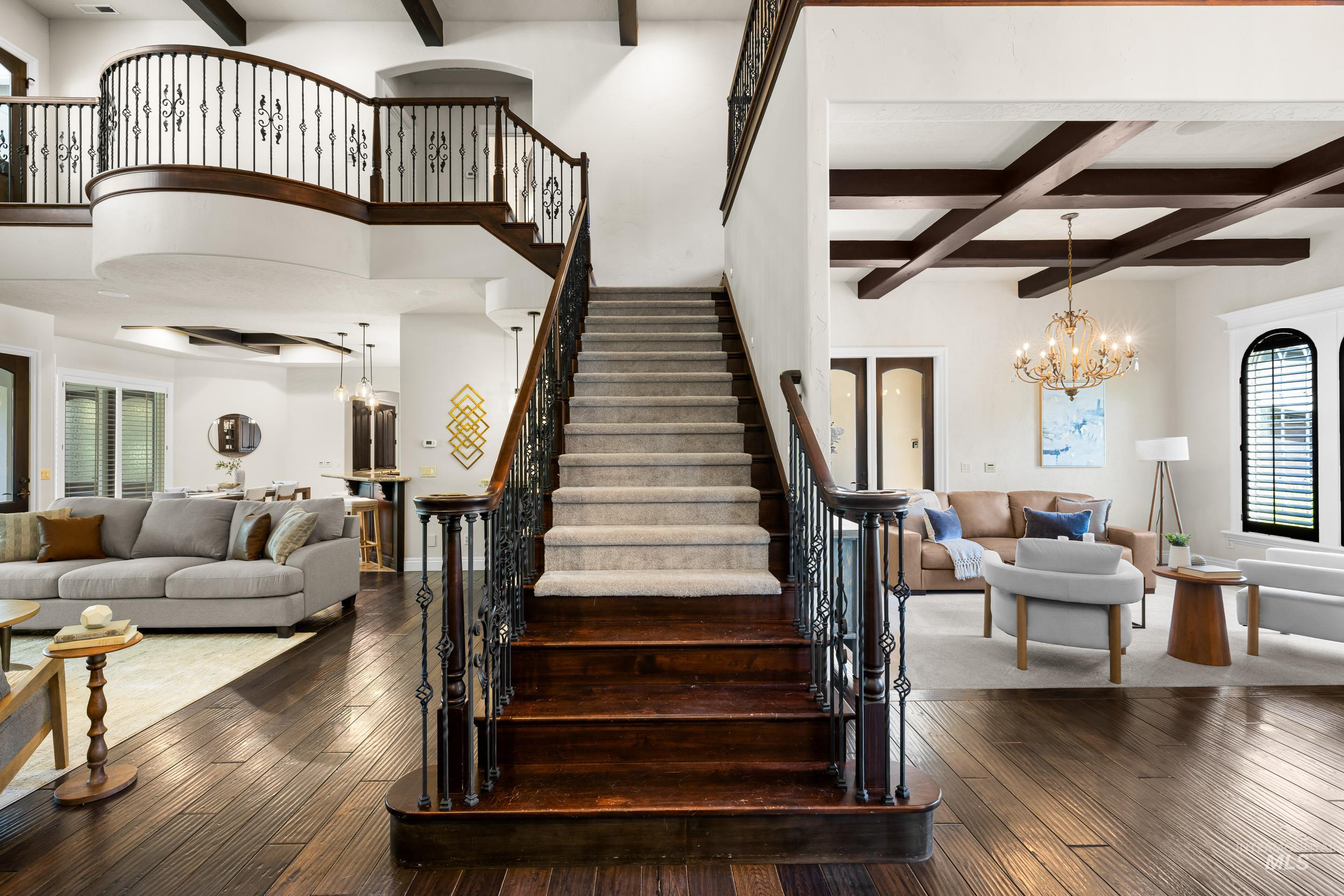 Staircase featuring beam ceiling, healthy amount of natural light, coffered ceiling, hardwood / wood-style flooring, and a chandelier