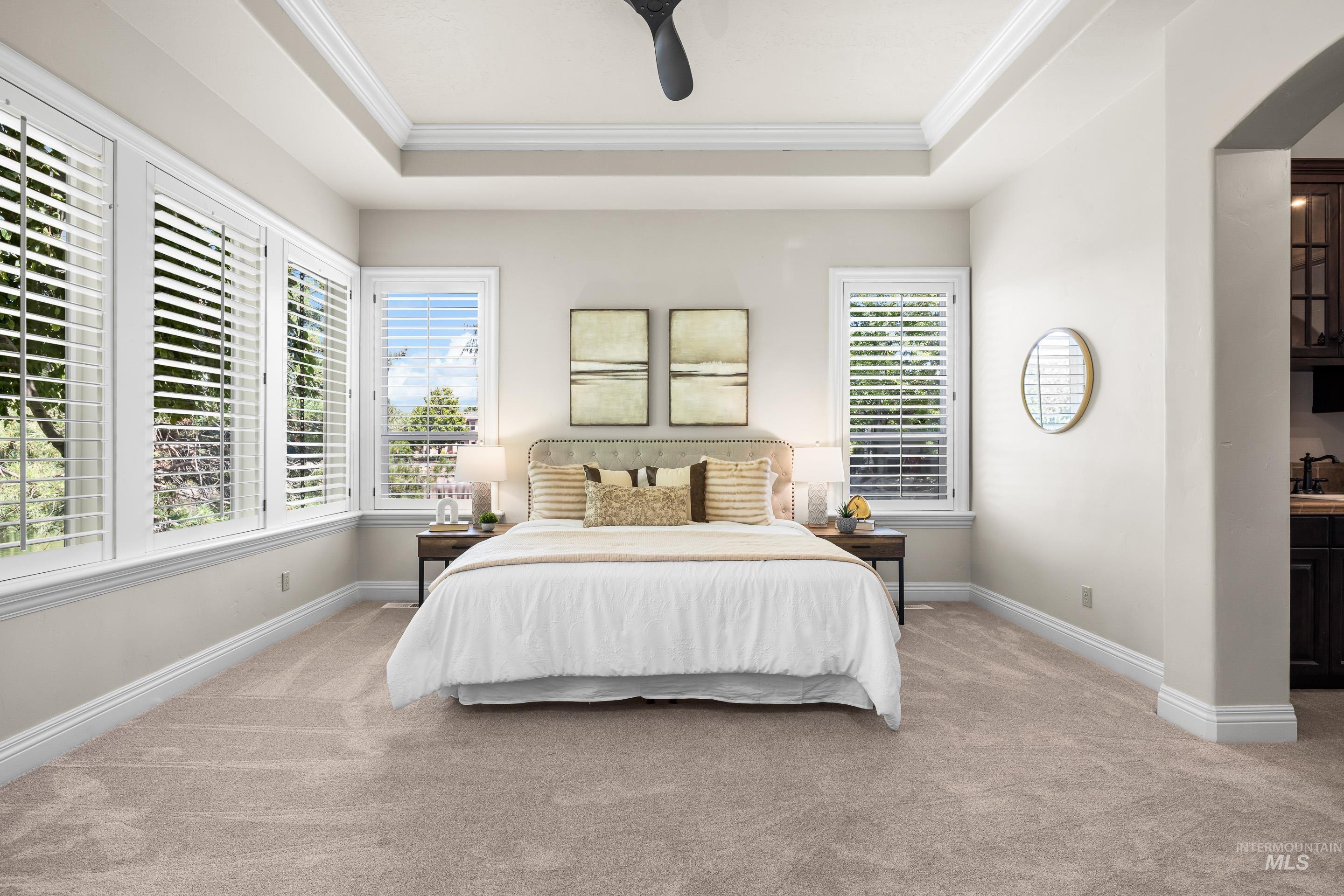 Bedroom featuring ornamental molding, carpet floors, a tray ceiling, and a ceiling fan