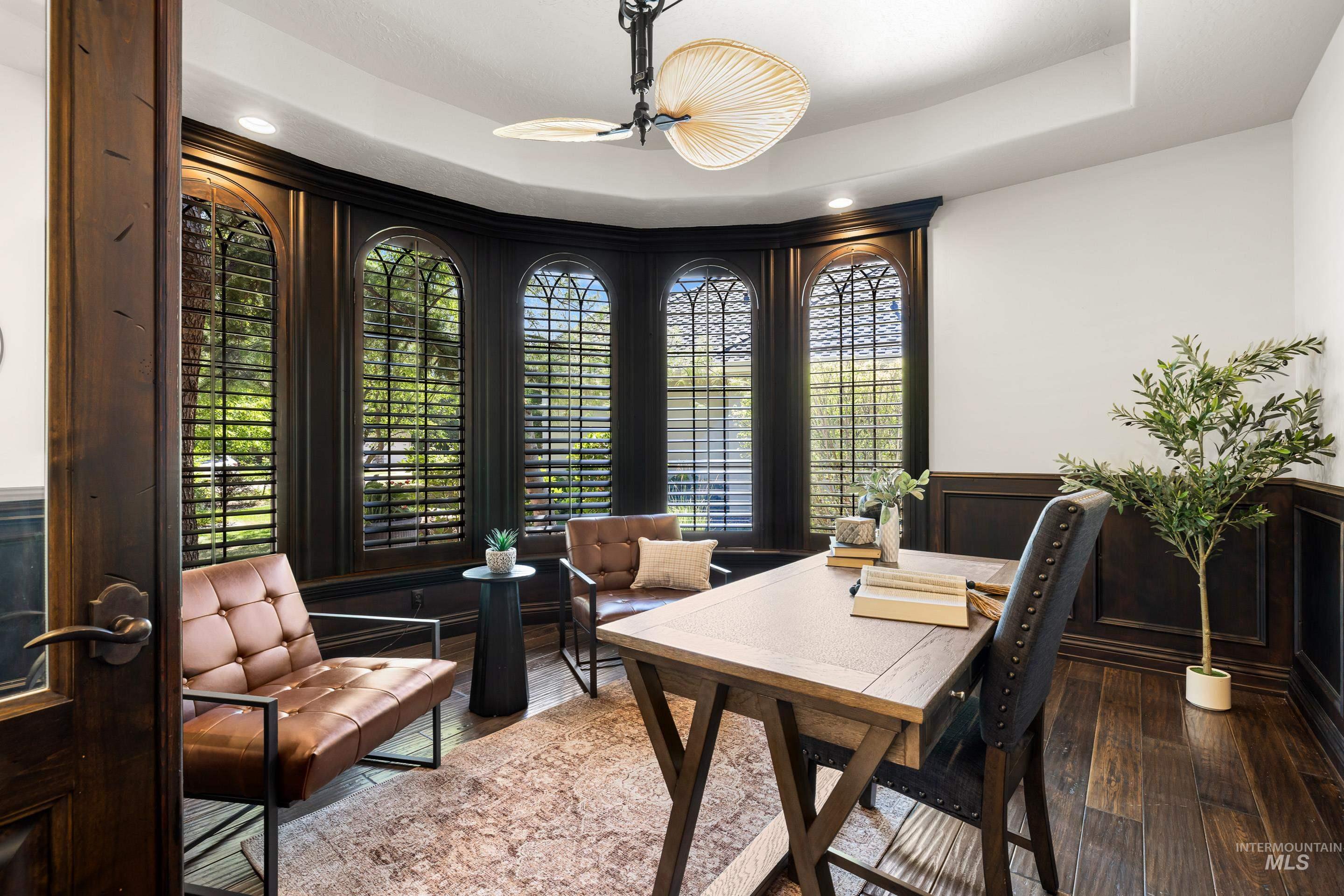 Home office featuring a wainscoted wall, a chandelier, wood-type flooring, a raised ceiling, and a decorative wall