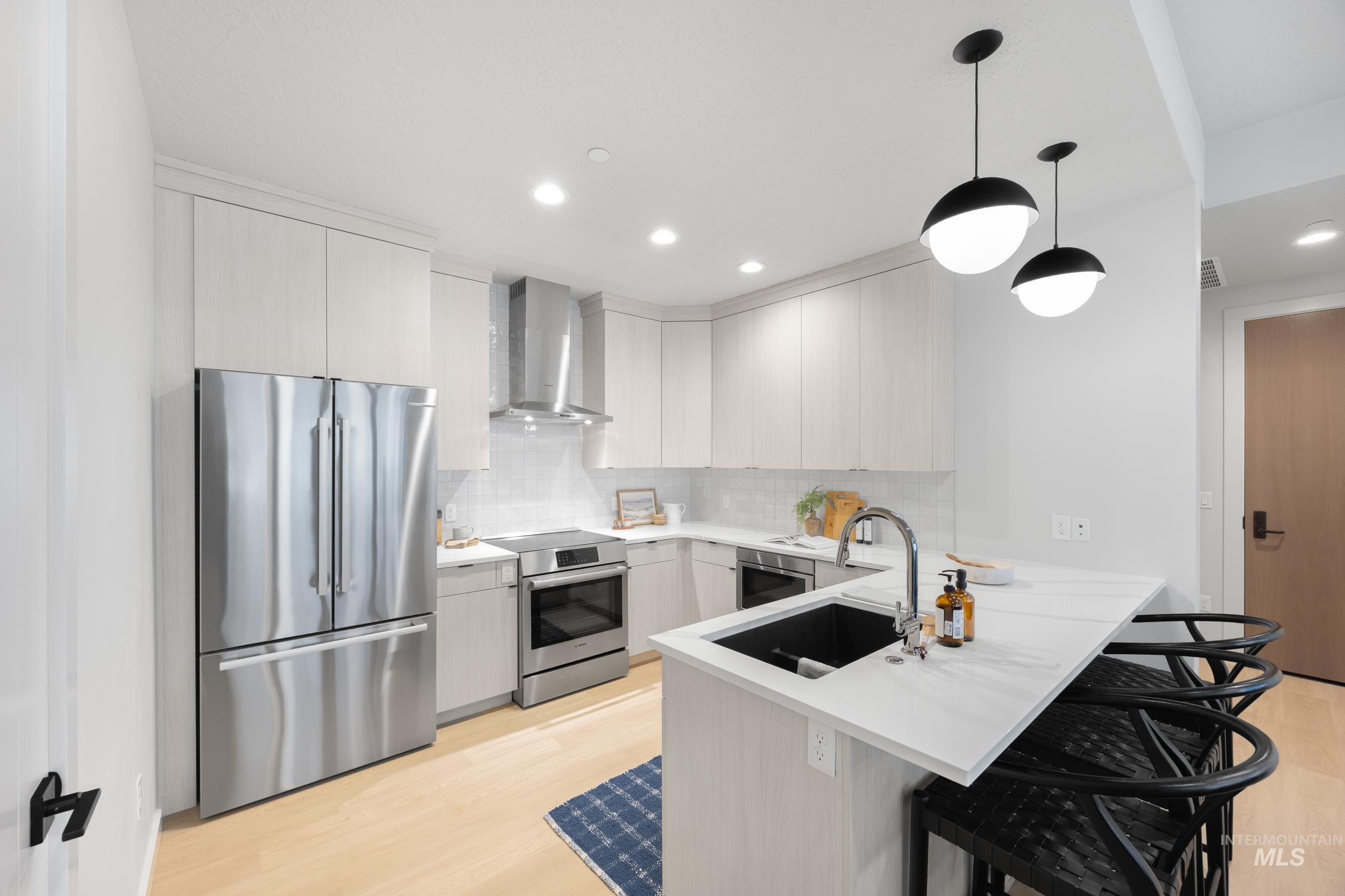 Kitchen featuring appliances with stainless steel finishes, a kitchen breakfast bar, a peninsula, decorative backsplash, and decorative light fixtures