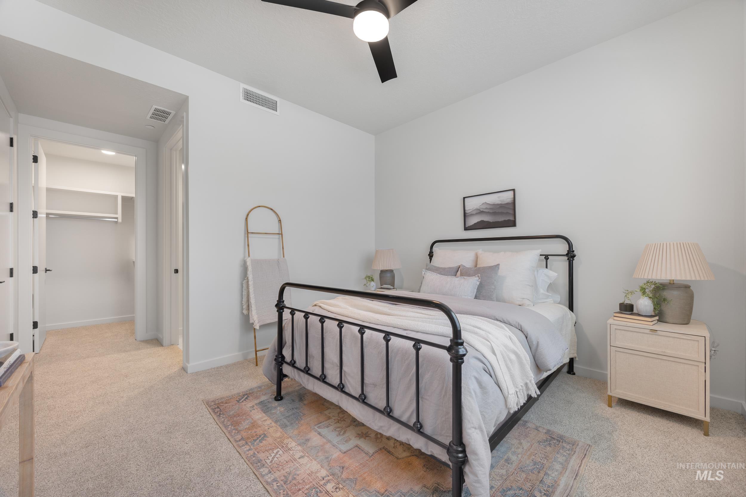Bedroom with a walk in closet, light carpet, and ceiling fan