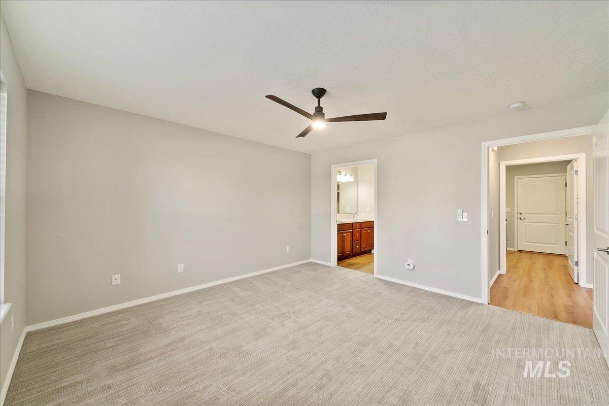 Unfurnished bedroom featuring a ceiling fan, light colored carpet, ensuite bathroom, and a textured ceiling