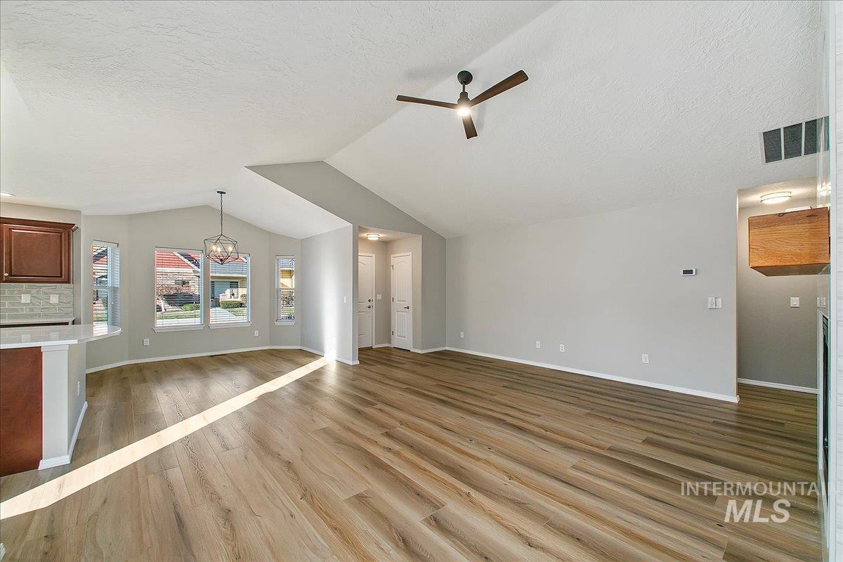 Unfurnished living room with light wood finished floors, a chandelier, lofted ceiling, ceiling fan, and a textured ceiling