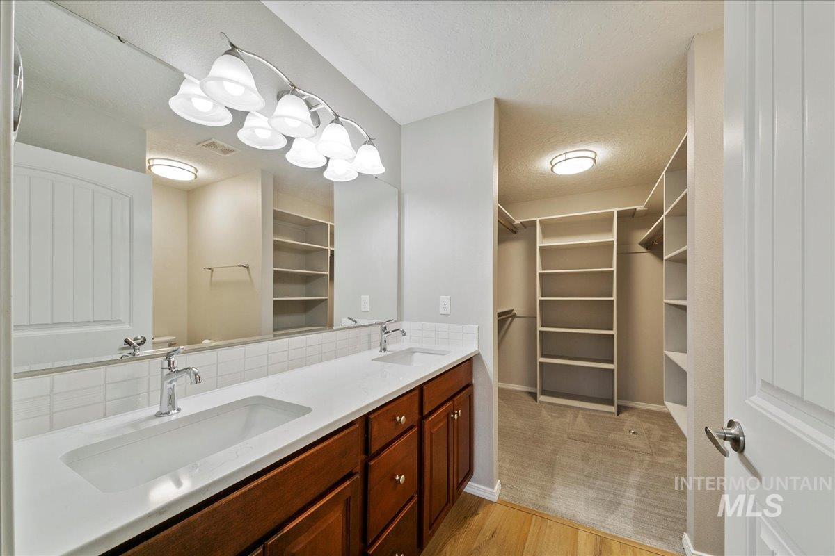 Bathroom with double vanity, a textured ceiling, a spacious closet, light colored carpet, and light wood-style flooring