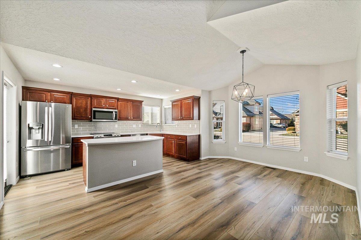 Kitchen with appliances with stainless steel finishes, plenty of natural light, a kitchen island, hanging light fixtures, and a textured ceiling