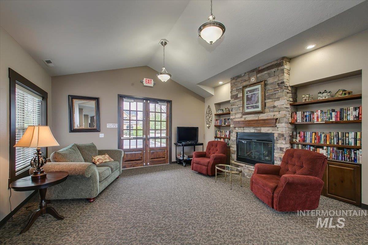 Living area with carpet flooring, vaulted ceiling, a stone fireplace, french doors, and built in features