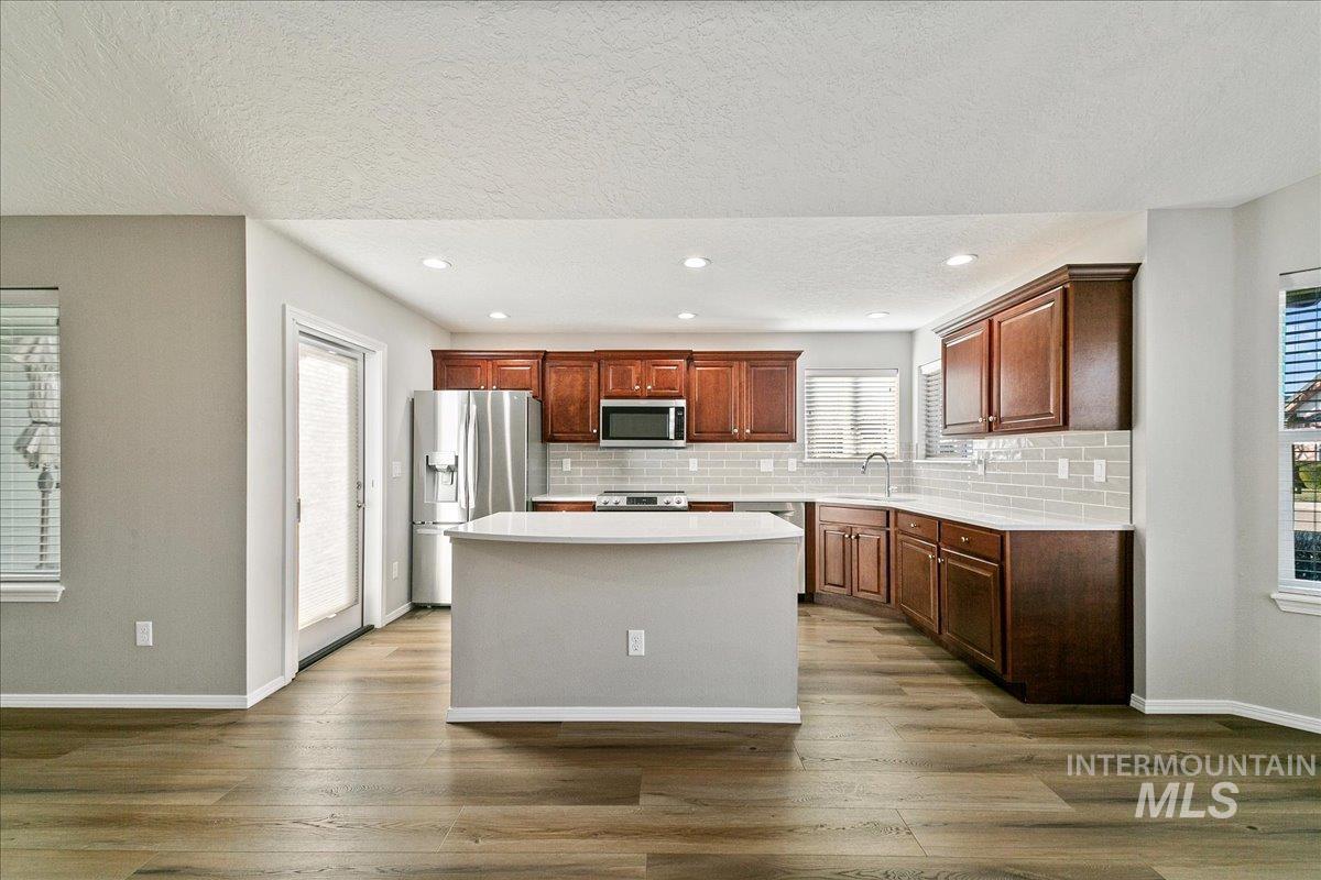 Kitchen with appliances with stainless steel finishes, a center island, tasteful backsplash, dark wood-type flooring, and recessed lighting