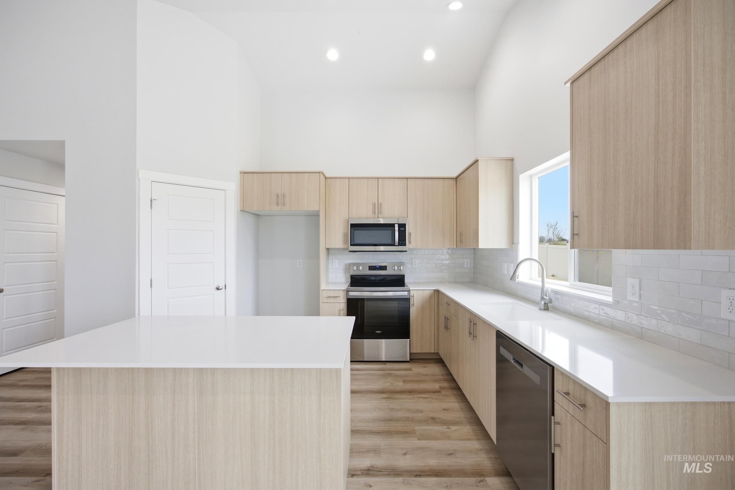Kitchen featuring light wood-finish cabinetry, white countertops, stainless steel appliances, and a subway tile backsplash