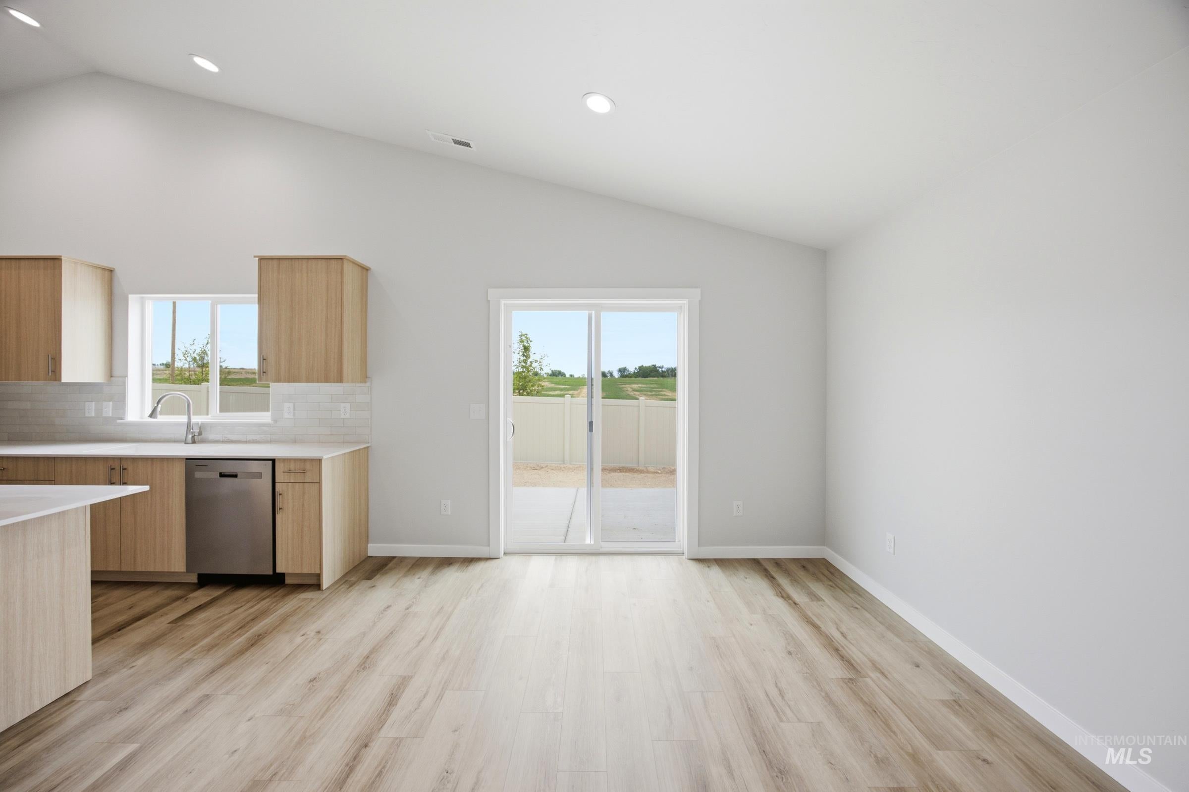Open-concept living area featuring a vaulted ceiling with recessed lighting, wood-finish flooring, and a kitchen with light wood-tone cabinetry