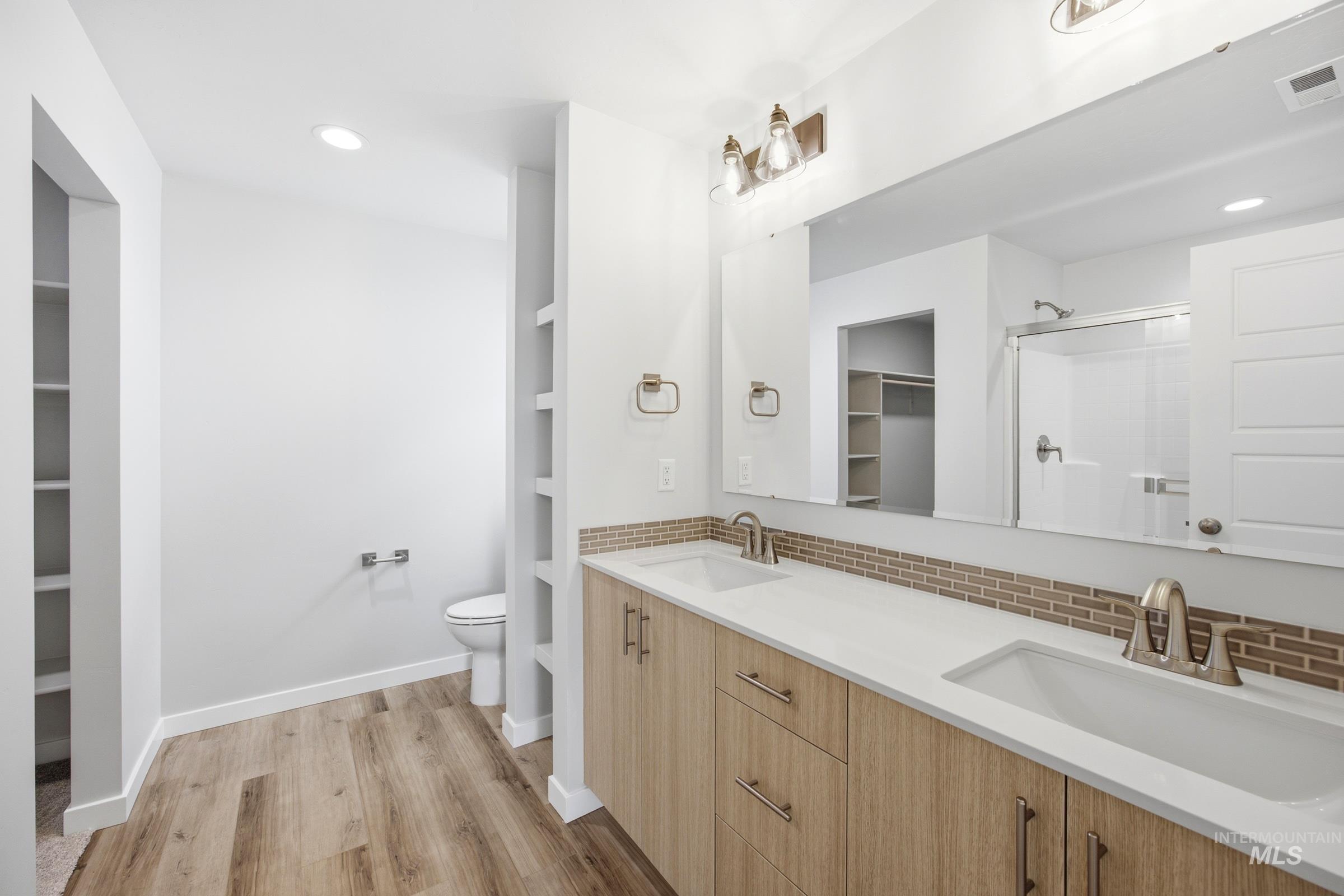 Bathroom featuring a dual vanity with light wood-finish cabinetry, white countertops, and a full-width mirror