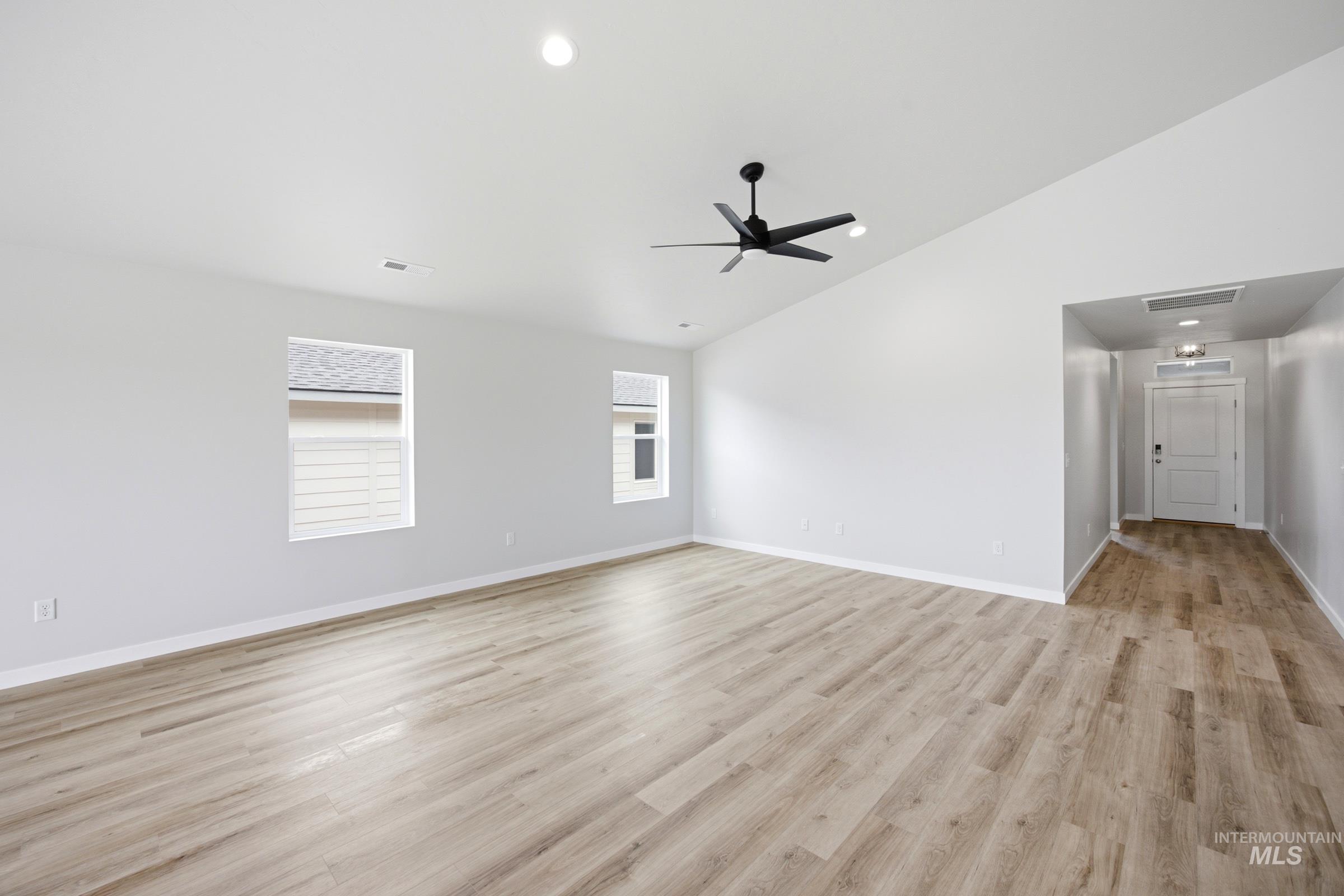 Spacious room featuring vaulted ceilings, wood-finish flooring, recessed lighting, a modern ceiling fan, and multiple windows