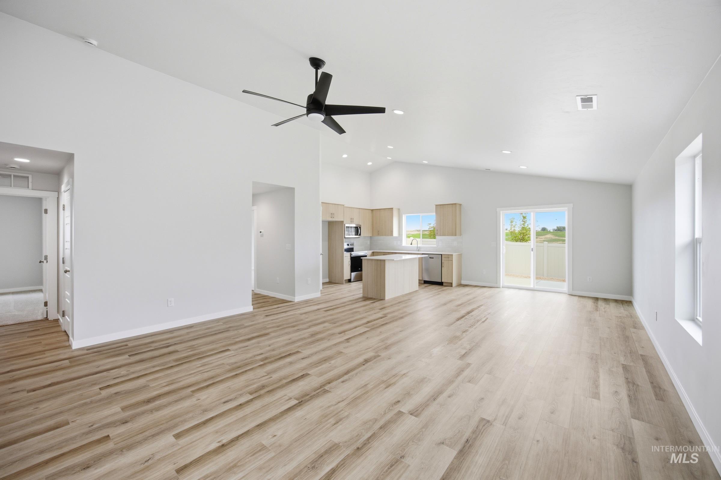 Spacious open-concept living area featuring wood-finish flooring, vaulted ceilings, and recessed lighting