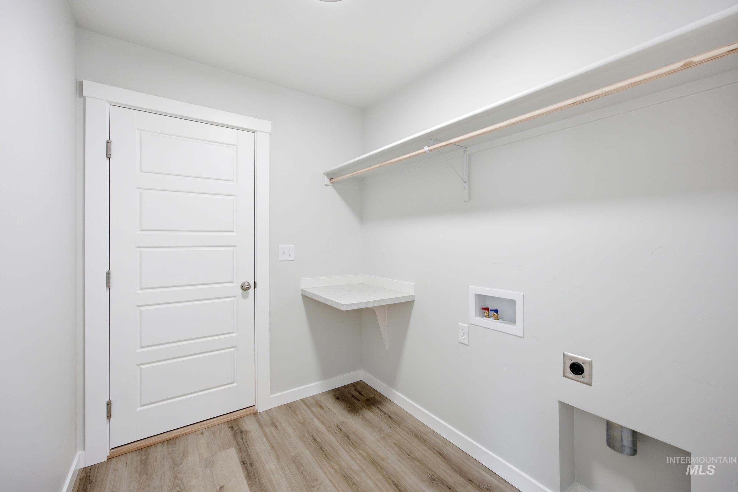 Laundry room featuring wood-finish flooring, a built-in countertop, and a wall-mounted shelving unit