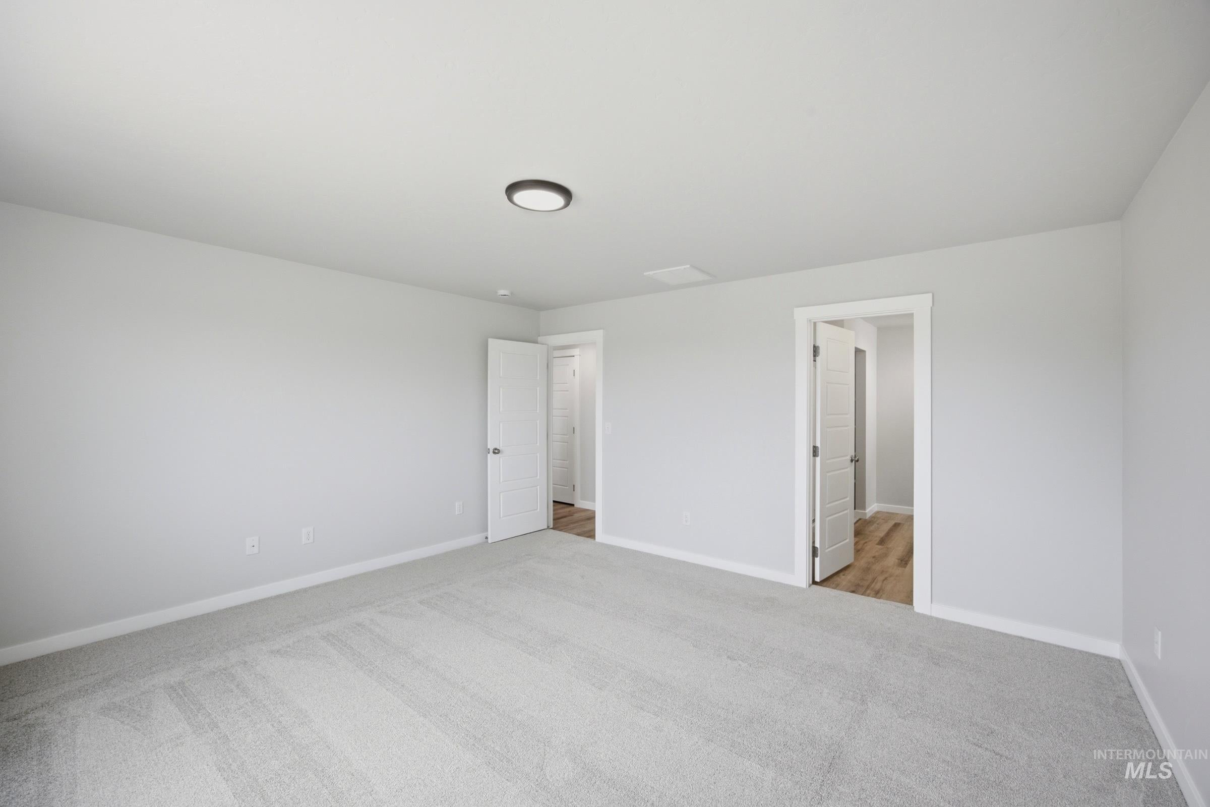 Spacious interior room featuring light gray carpeting, white baseboards, and neutral wall paint