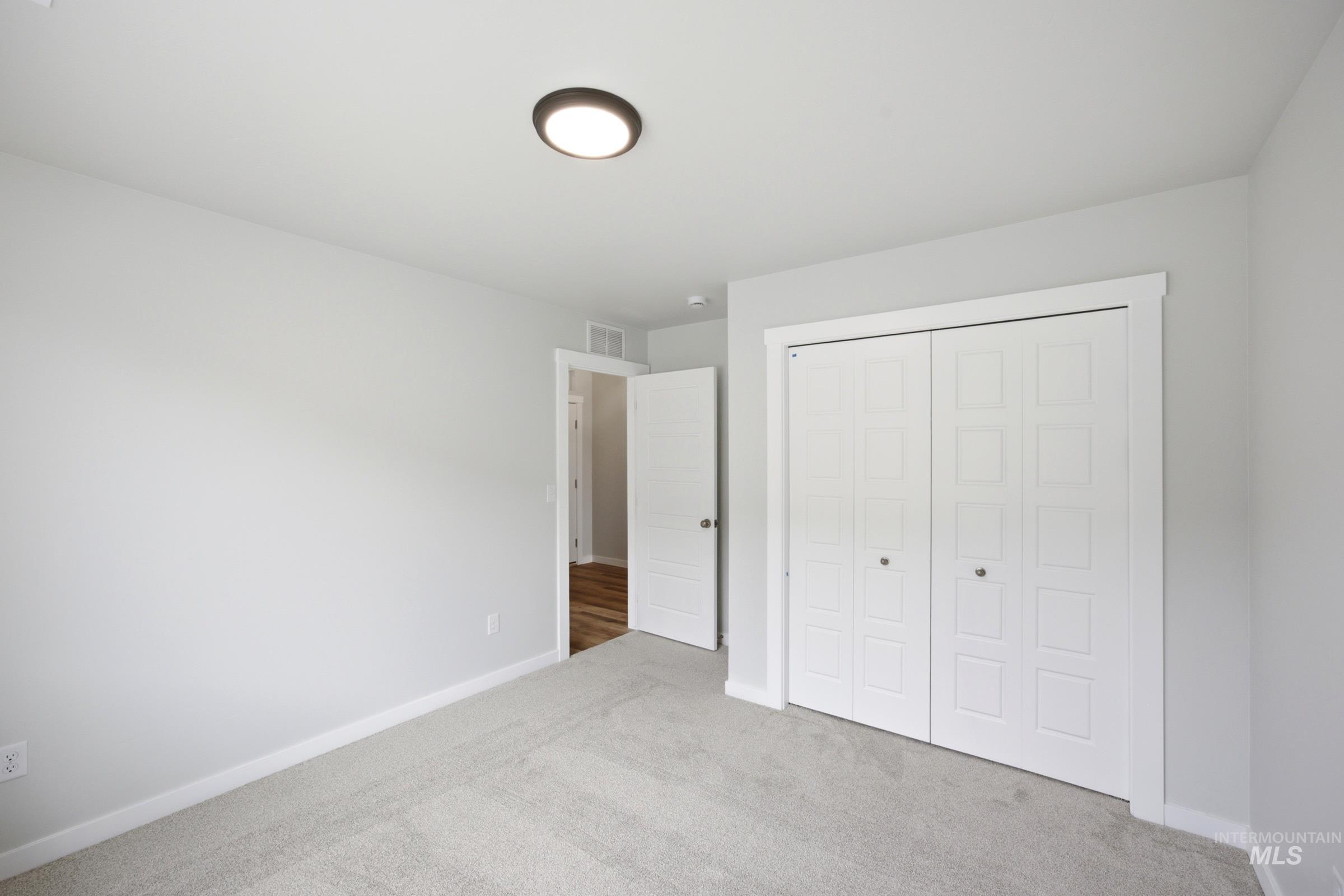 Room featuring light grey wall paint, light grey carpet flooring, white baseboards, and a white bi-fold closet