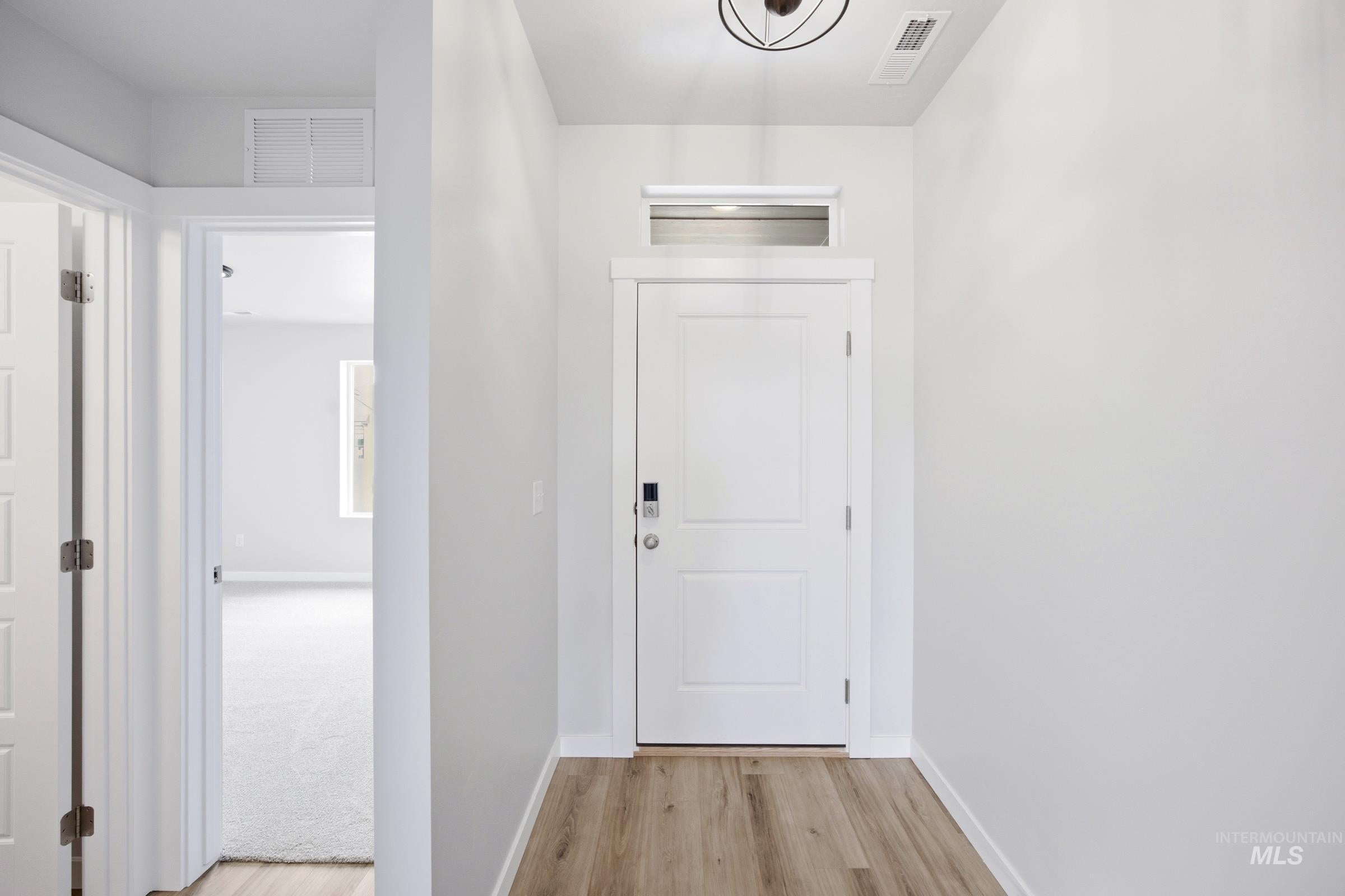 Entryway featuring wood-finish flooring, a white paneled door with transom window, and a contemporary ceiling light fixture