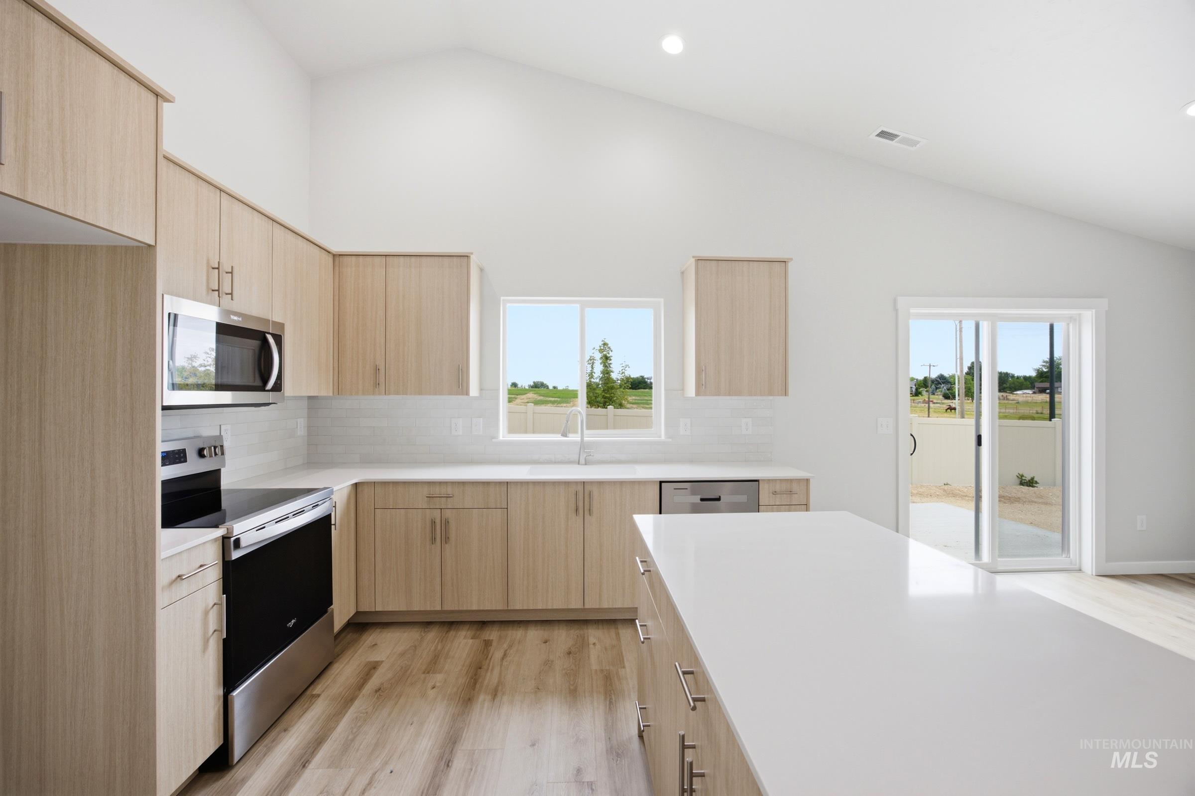 Modern kitchen featuring light wood-finish cabinetry, stainless steel appliances, and a central island with a white countertop