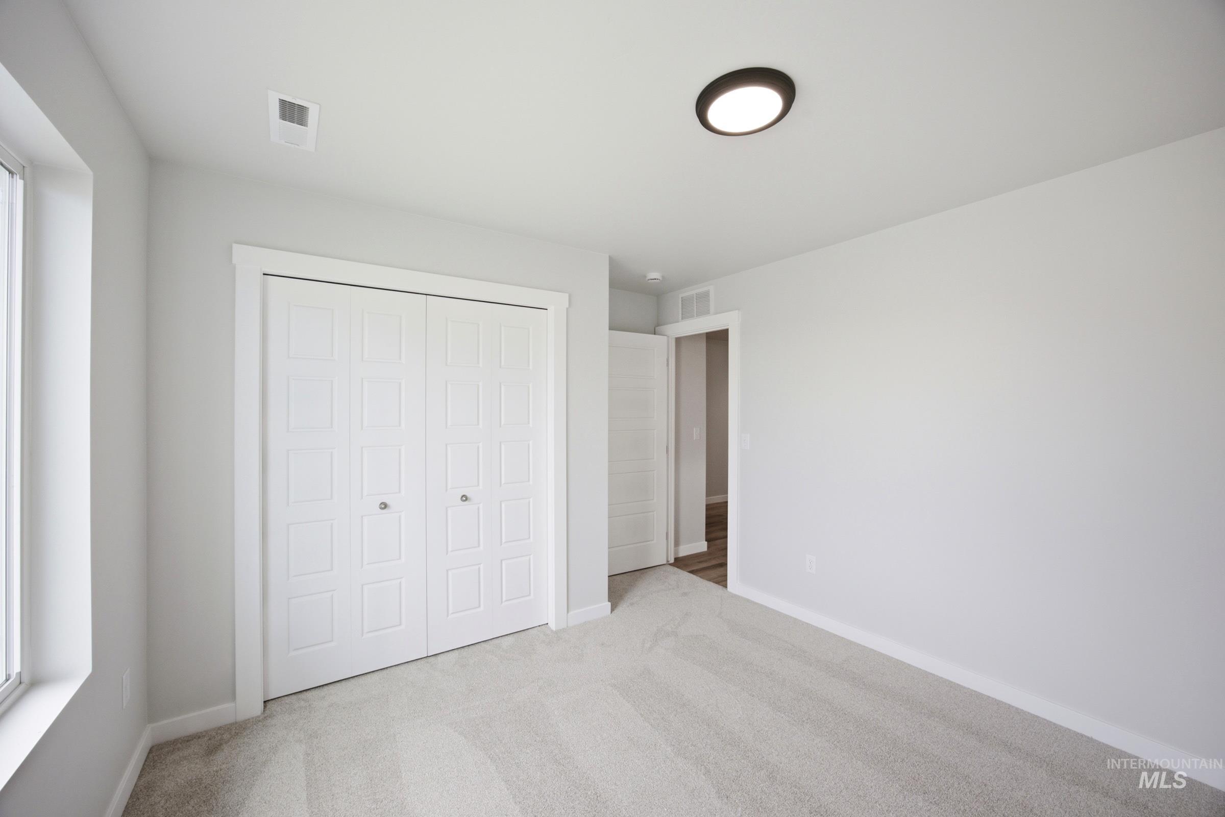 Room featuring a window, light gray walls, carpet flooring, a flush-mount ceiling light, and white bi-fold closet doors