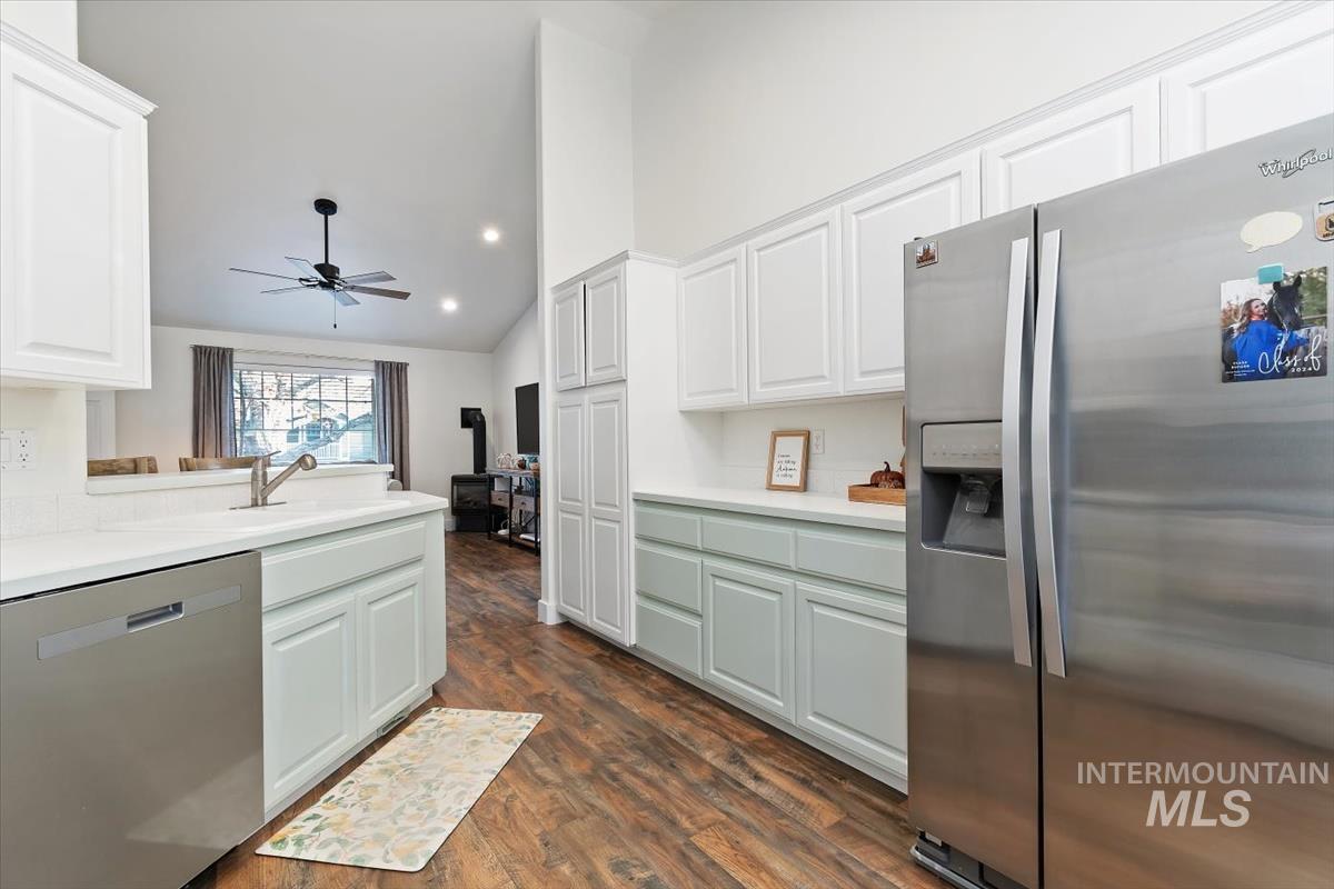 Kitchen with stainless steel appliances, white cabinetry, vaulted ceiling, light countertops, and dark wood-type flooring