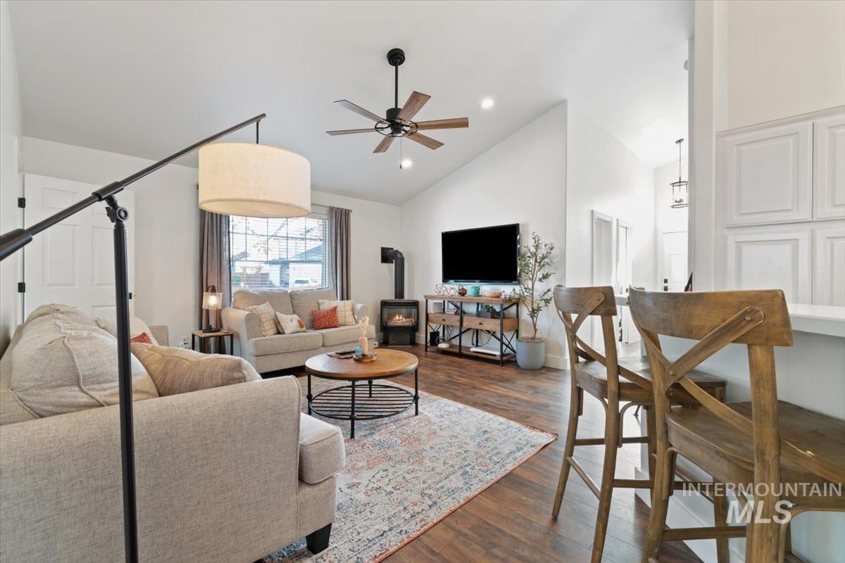 Living room with a wood stove, dark wood-style floors, a ceiling fan, high vaulted ceiling, and recessed lighting