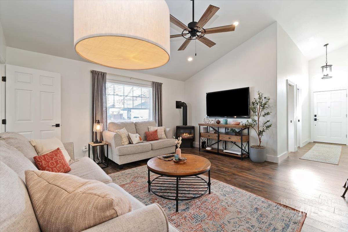 Living room with a wood stove, a ceiling fan, high vaulted ceiling, recessed lighting, and wood finished floors
