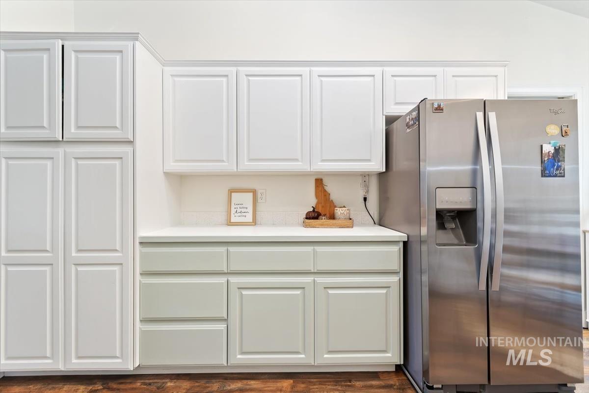 Kitchen with stainless steel fridge, white cabinets, and dark wood finished floors