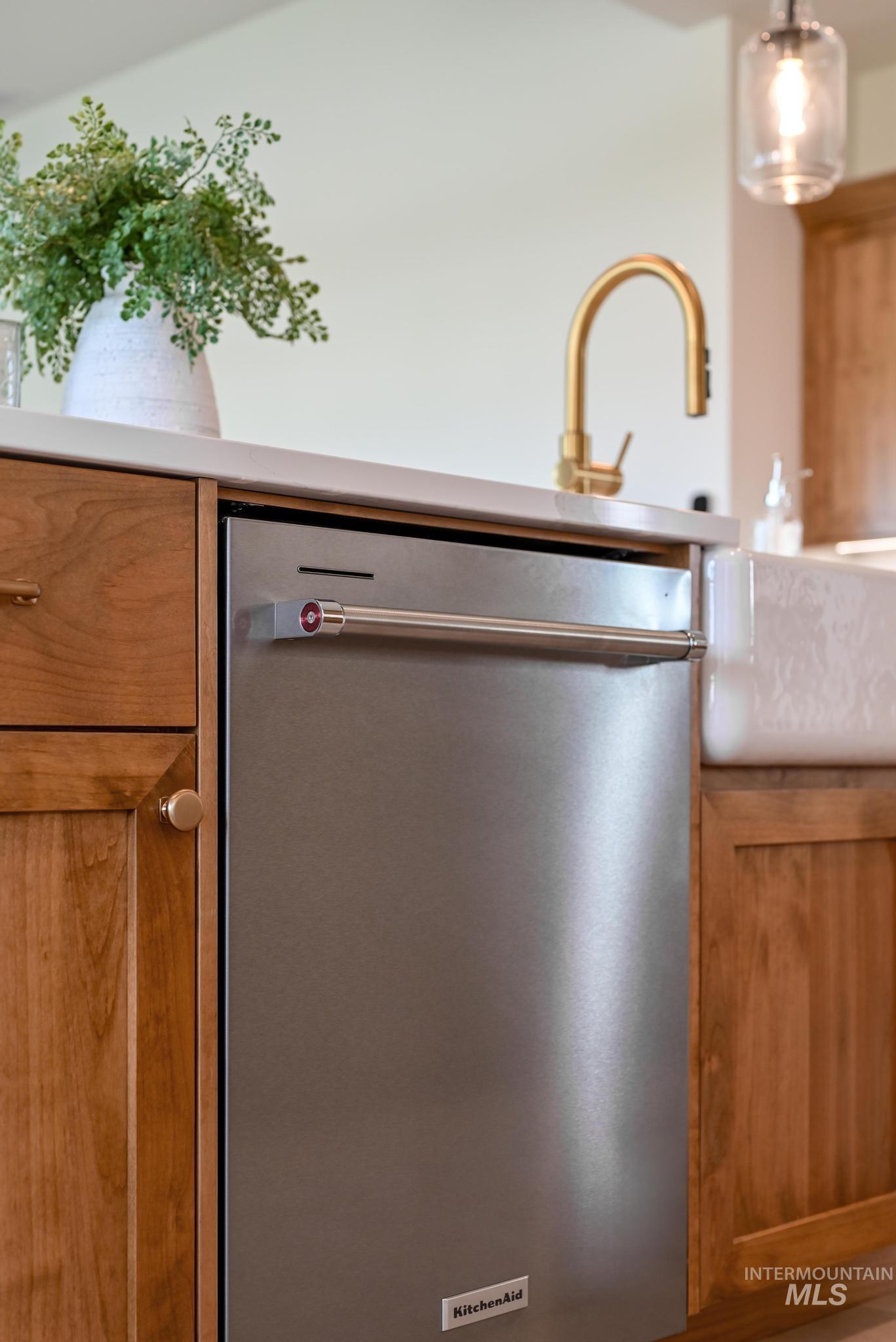 Kitchen view of stainless steel dishwasher, brown cabinets, light countertops, and pendant lighting