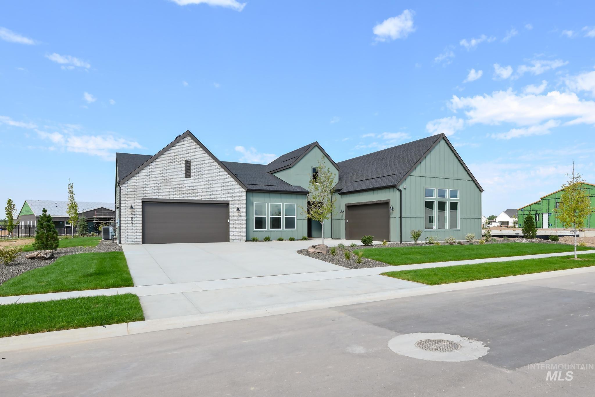 Modern farmhouse featuring a front lawn, driveway, board and batten siding, an attached garage, and brick siding