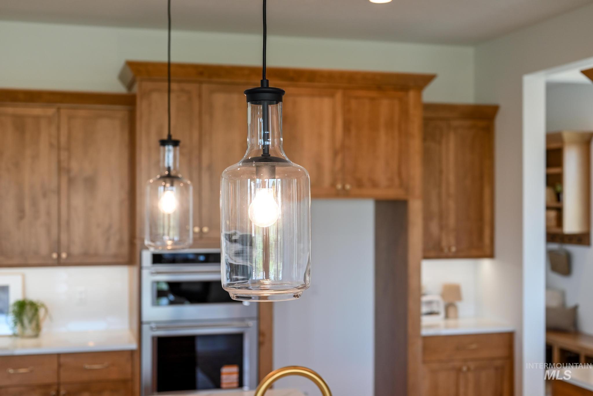 Kitchen with brown cabinetry, double oven, light countertops, and pendant lighting