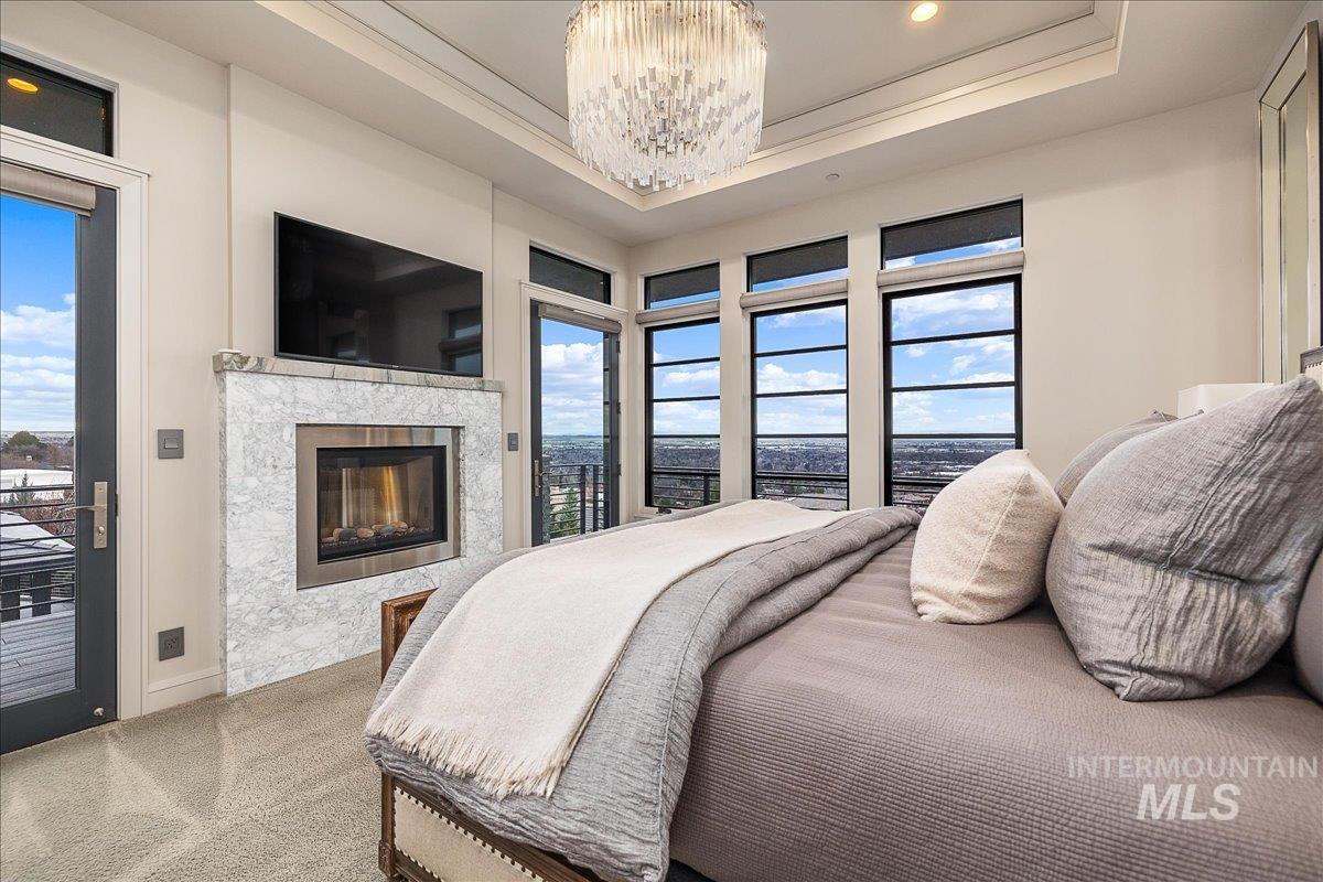 Bedroom with access to outside, a chandelier, a fireplace, carpet, and a tray ceiling