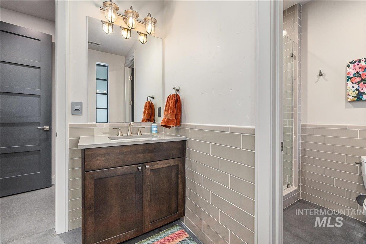 Full bathroom with vanity, a wainscoted wall, tile walls, and a stall shower