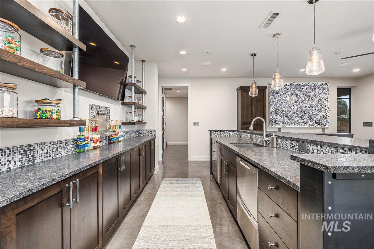 Kitchen featuring dark brown cabinetry, hanging light fixtures, dishwasher, dark stone counters, and decorative backsplash