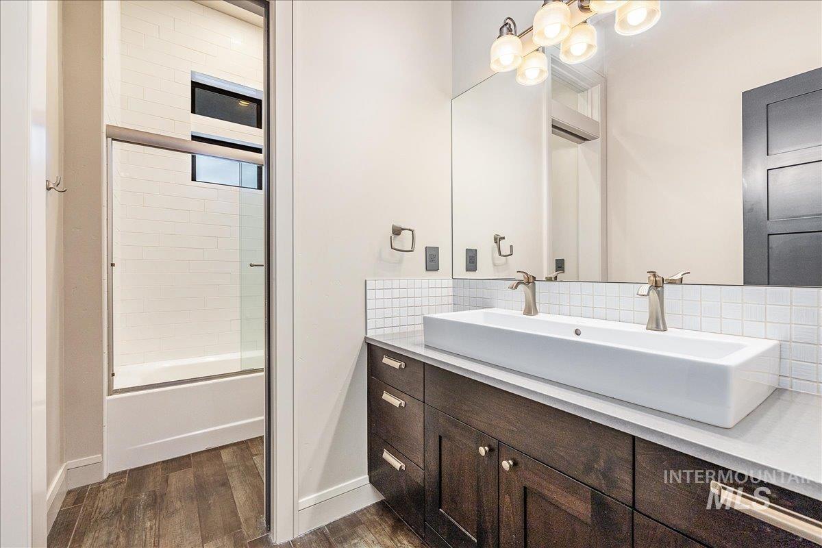 Bathroom featuring double vanity, decorative backsplash, dark wood-style floors, and enclosed tub / shower combo