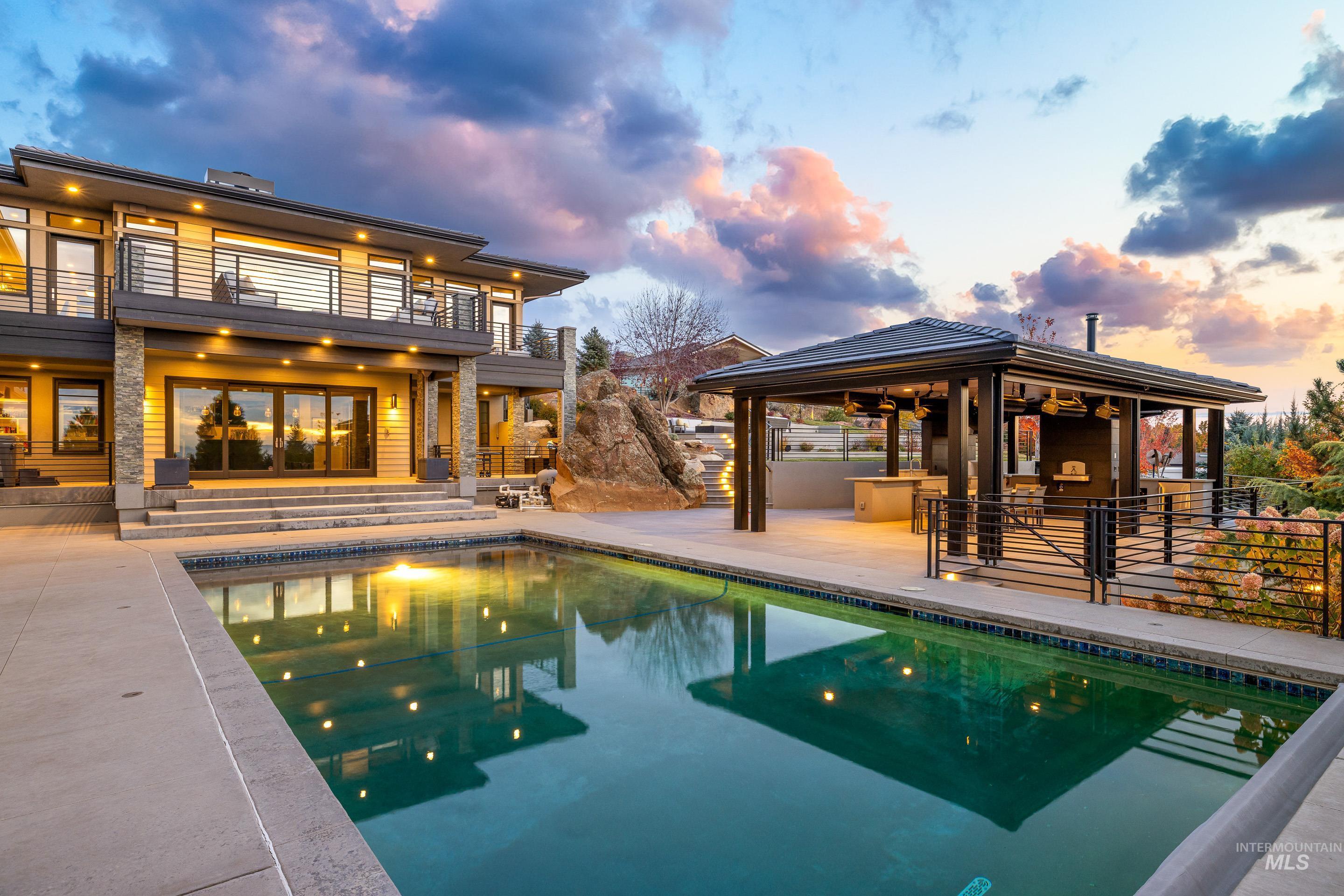 Back of house at dusk with a patio area, an outdoor pool, and a balcony