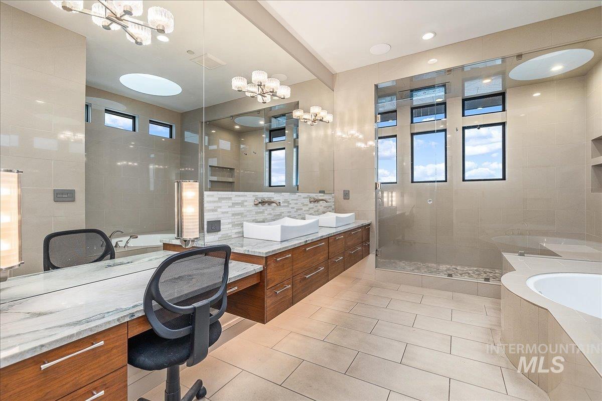 Bathroom with a garden tub, double vanity, a shower stall, a chandelier, and tile walls