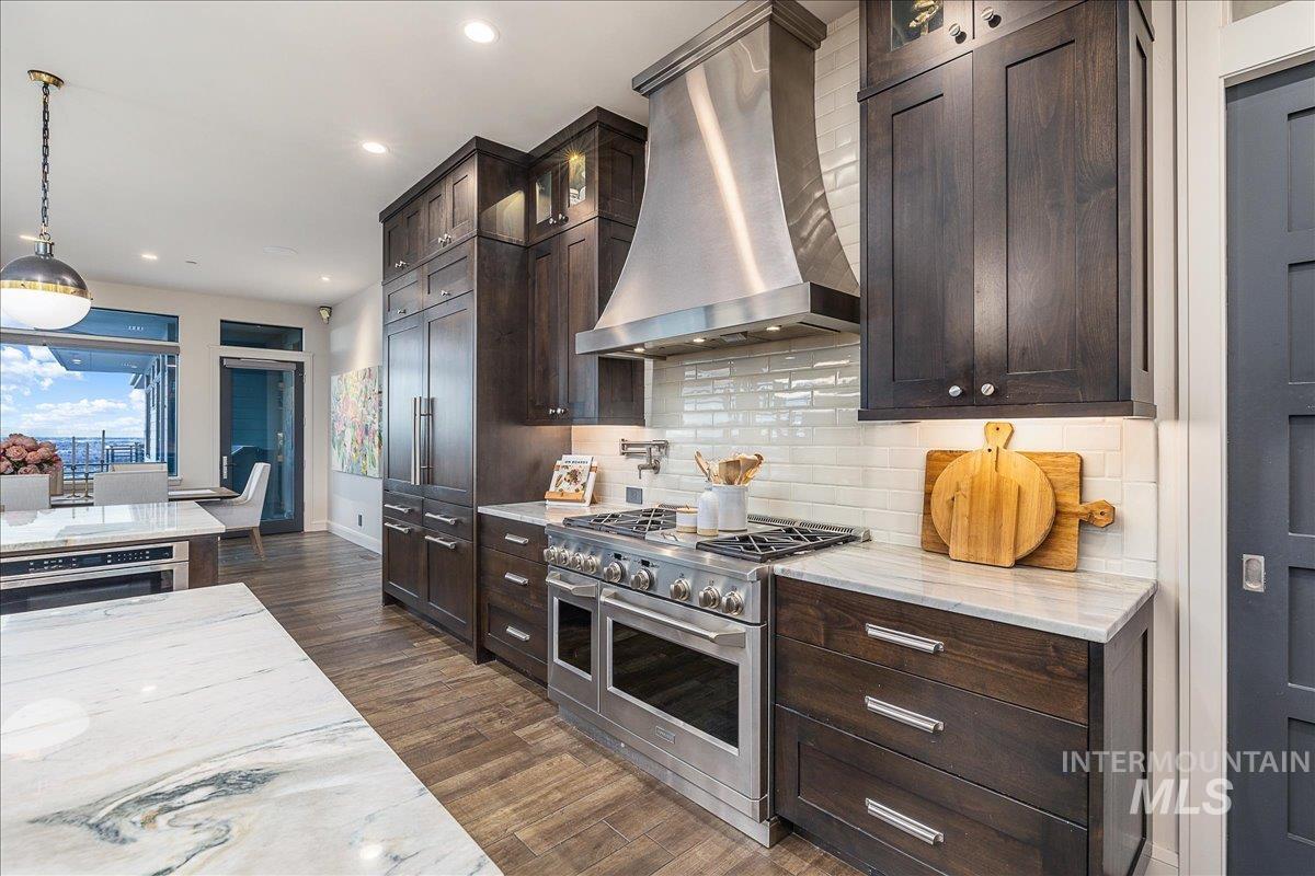 Kitchen featuring exhaust hood, high end appliances, light stone counters, decorative light fixtures, and glass insert cabinets