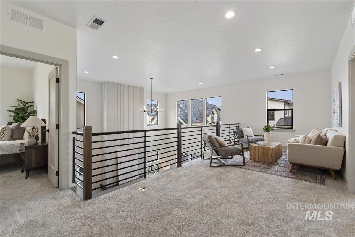 Living area with an upstairs landing, light colored carpet, and hanging lights