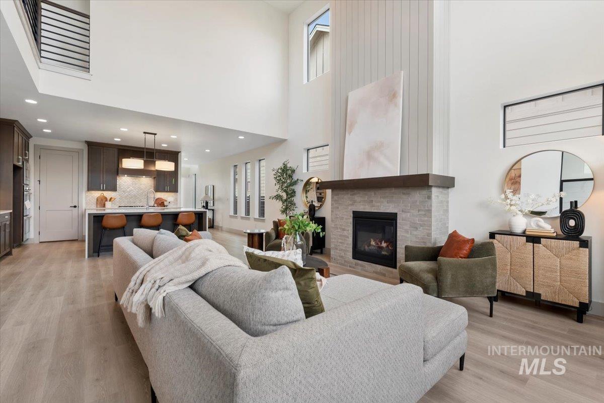 Living room featuring light wood finished floors, a brick fireplace, a high ceiling, and recessed lighting