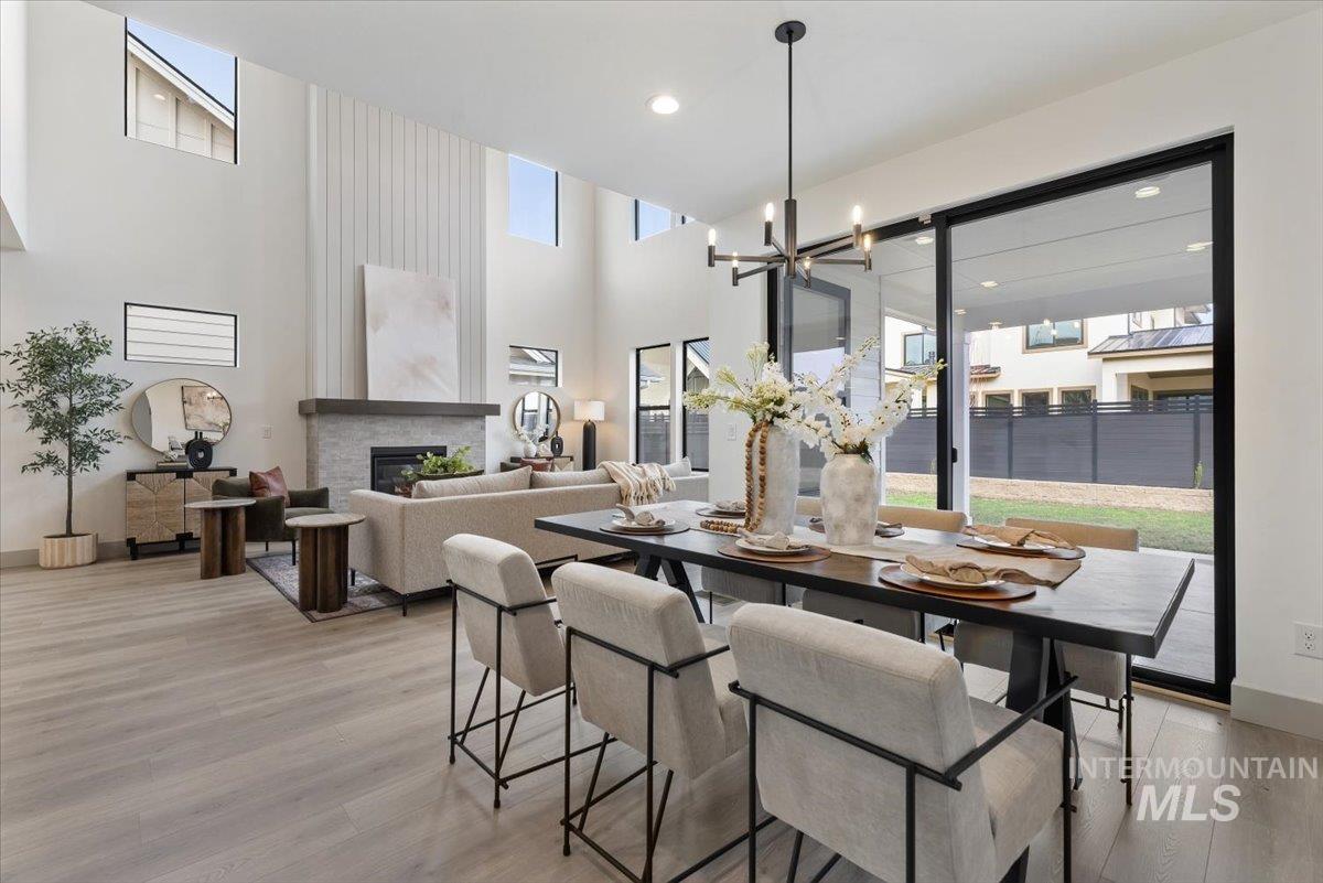 Dining area with light wood-style flooring, a glass covered fireplace, a high ceiling, and suspended lighting