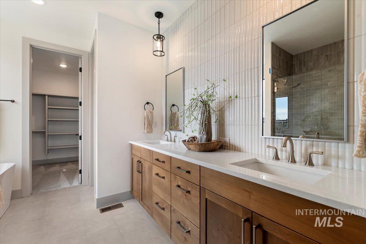 Bathroom featuring a stall shower, a spacious closet, double vanity, a freestanding tub, and light tile patterned floors