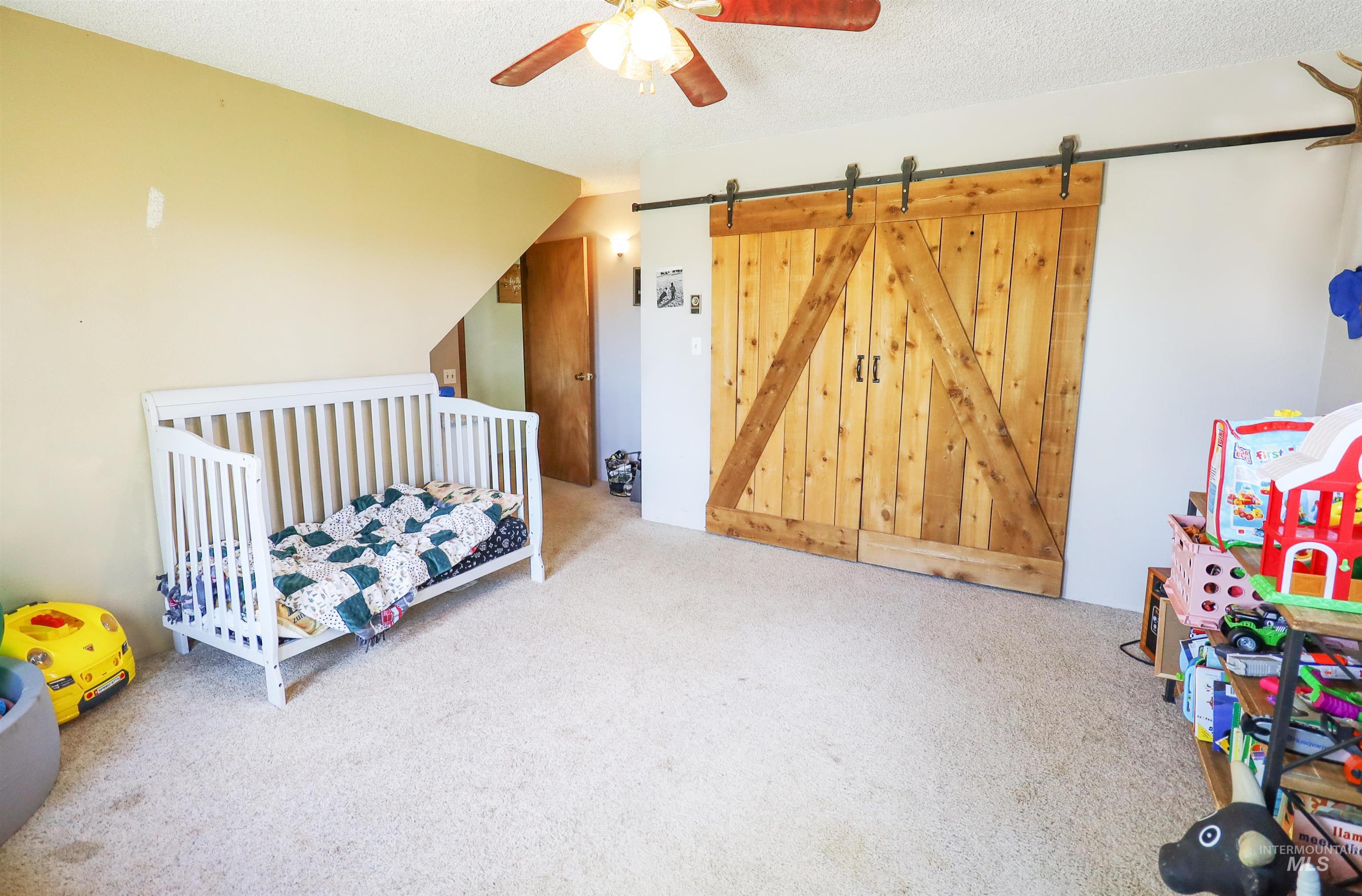 Carpeted bedroom with a barn door and ceiling fan