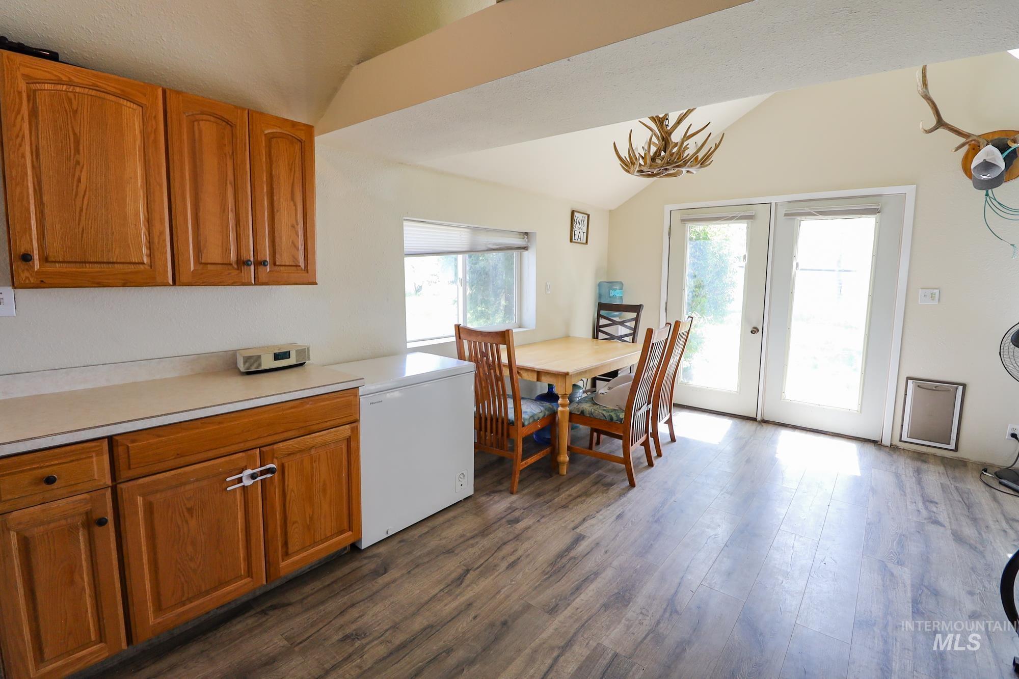 Kitchen featuring vaulted ceiling, fridge, brown cabinetry, dark wood finished floors, and light countertops