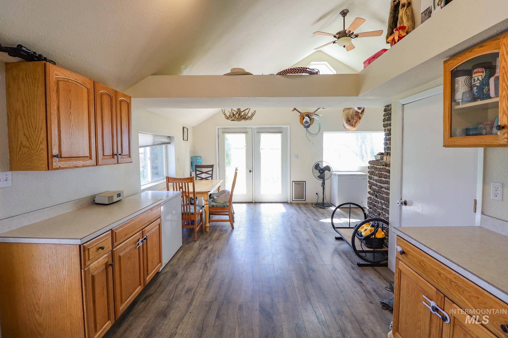 Kitchen featuring vaulted ceiling, light countertops, dark wood finished floors, ceiling fan, and glass insert cabinets