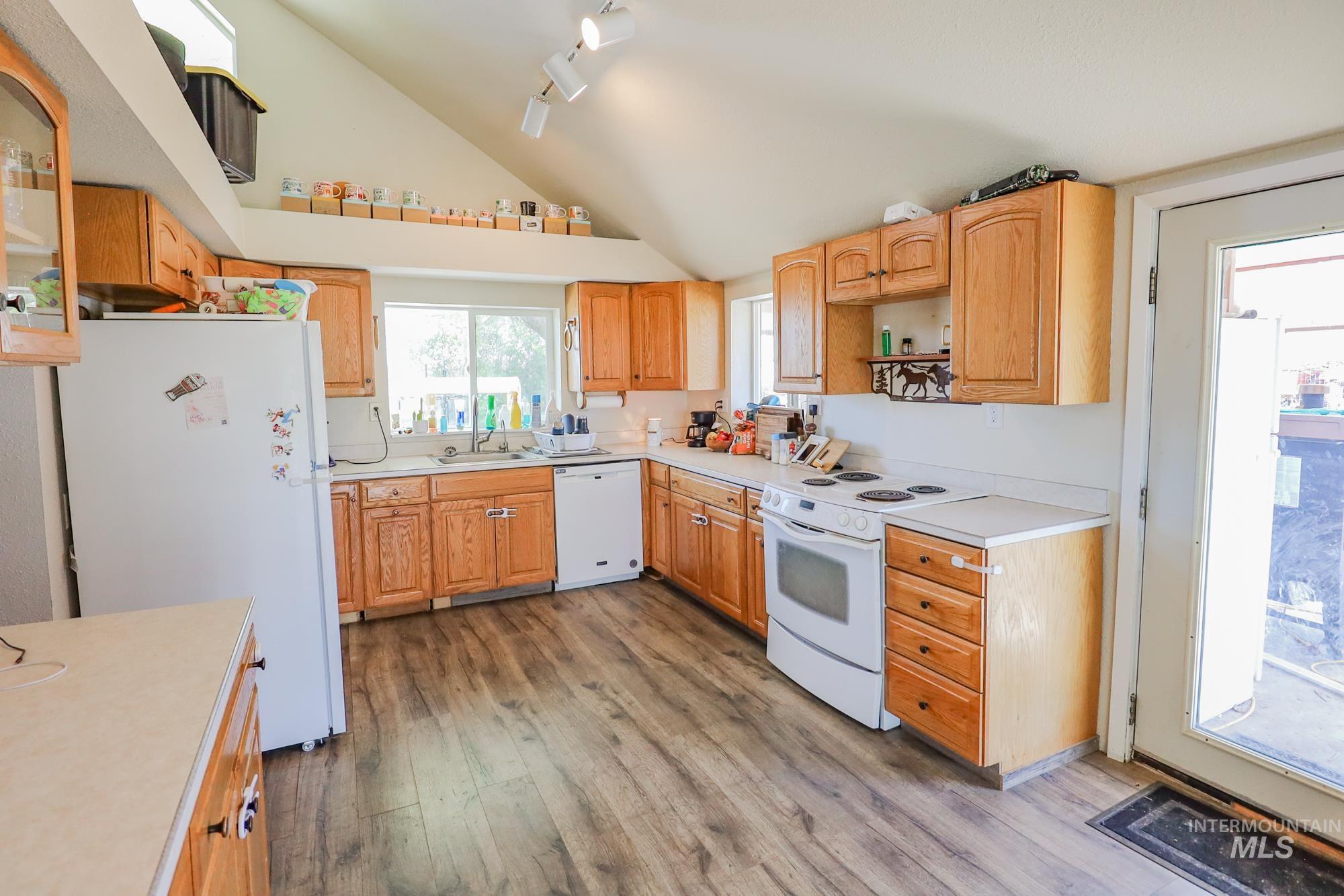 Kitchen featuring white appliances, light wood-style floors, lofted ceiling, light countertops, and track lighting