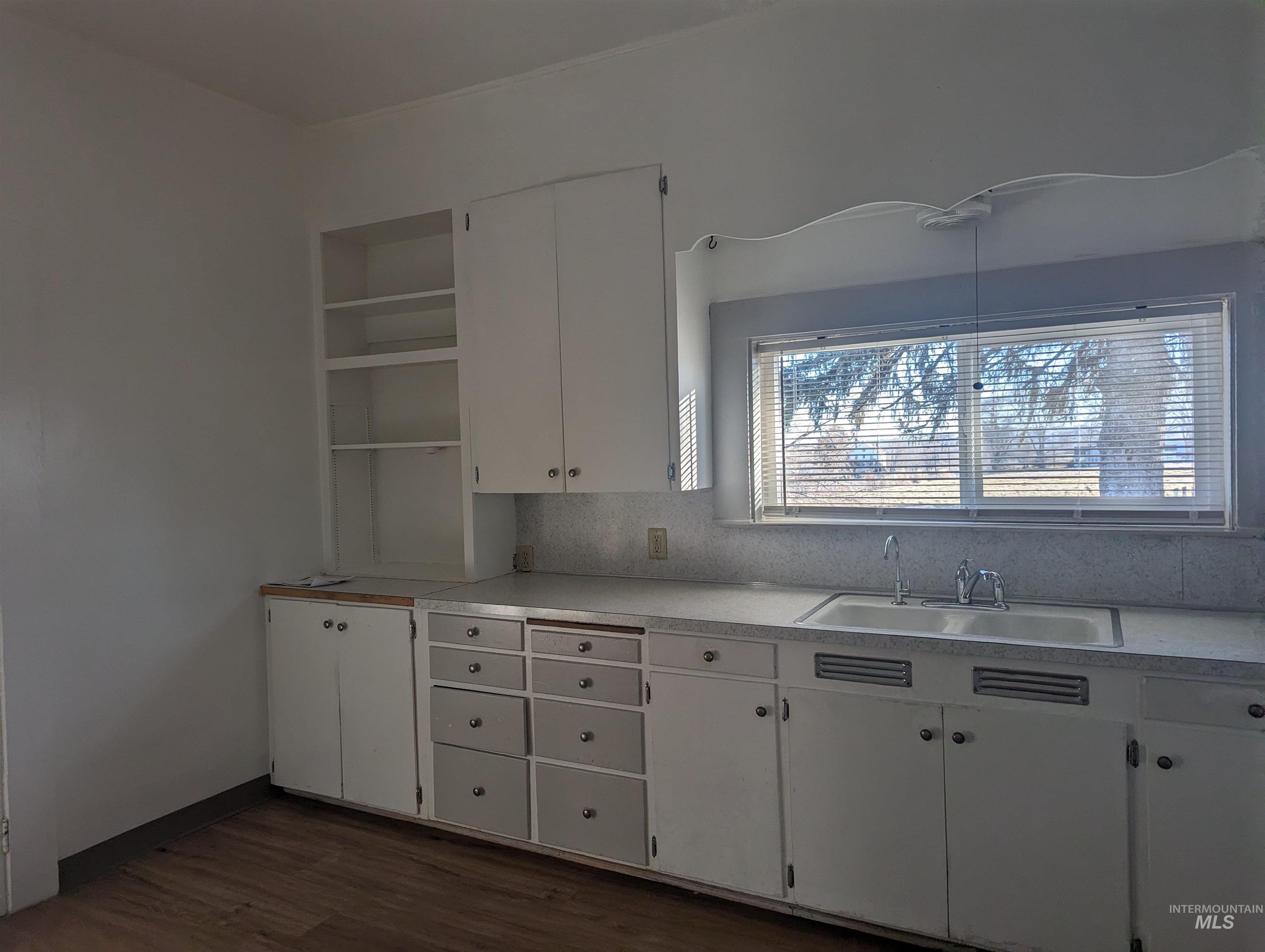 Kitchen with open shelves, white cabinets, light countertops, dark wood-type flooring, and backsplash