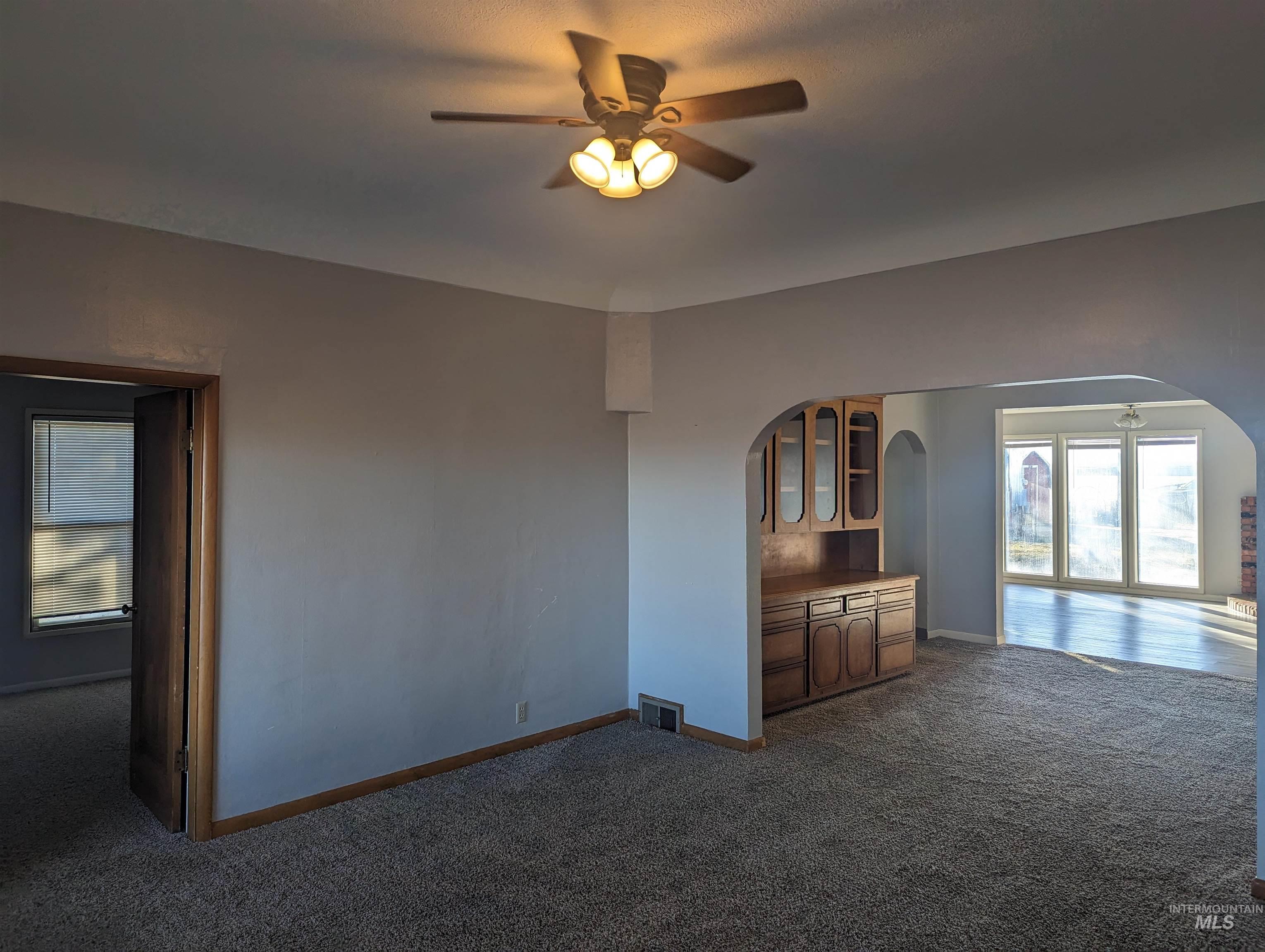 Unfurnished living room featuring ceiling fan, dark carpet, and arched walkways