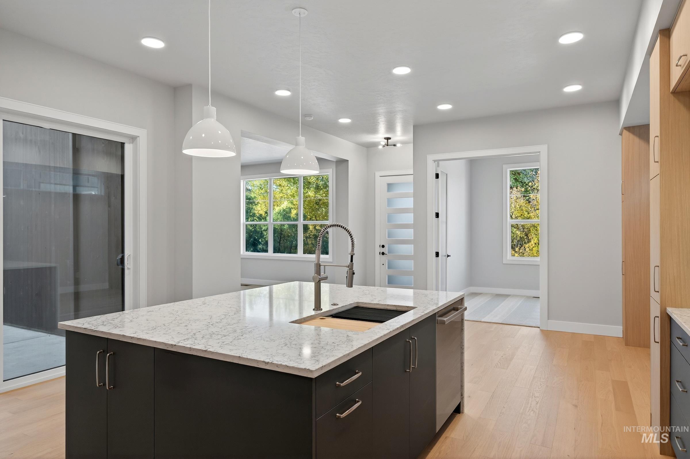 Kitchen featuring dark cabinetry, decorative light fixtures, light wood-style flooring, light stone countertops, and recessed lighting