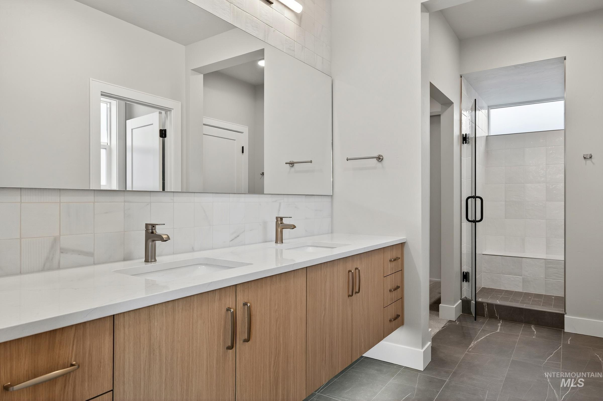 Bathroom featuring double vanity, backsplash, a stall shower, and dark tile patterned flooring