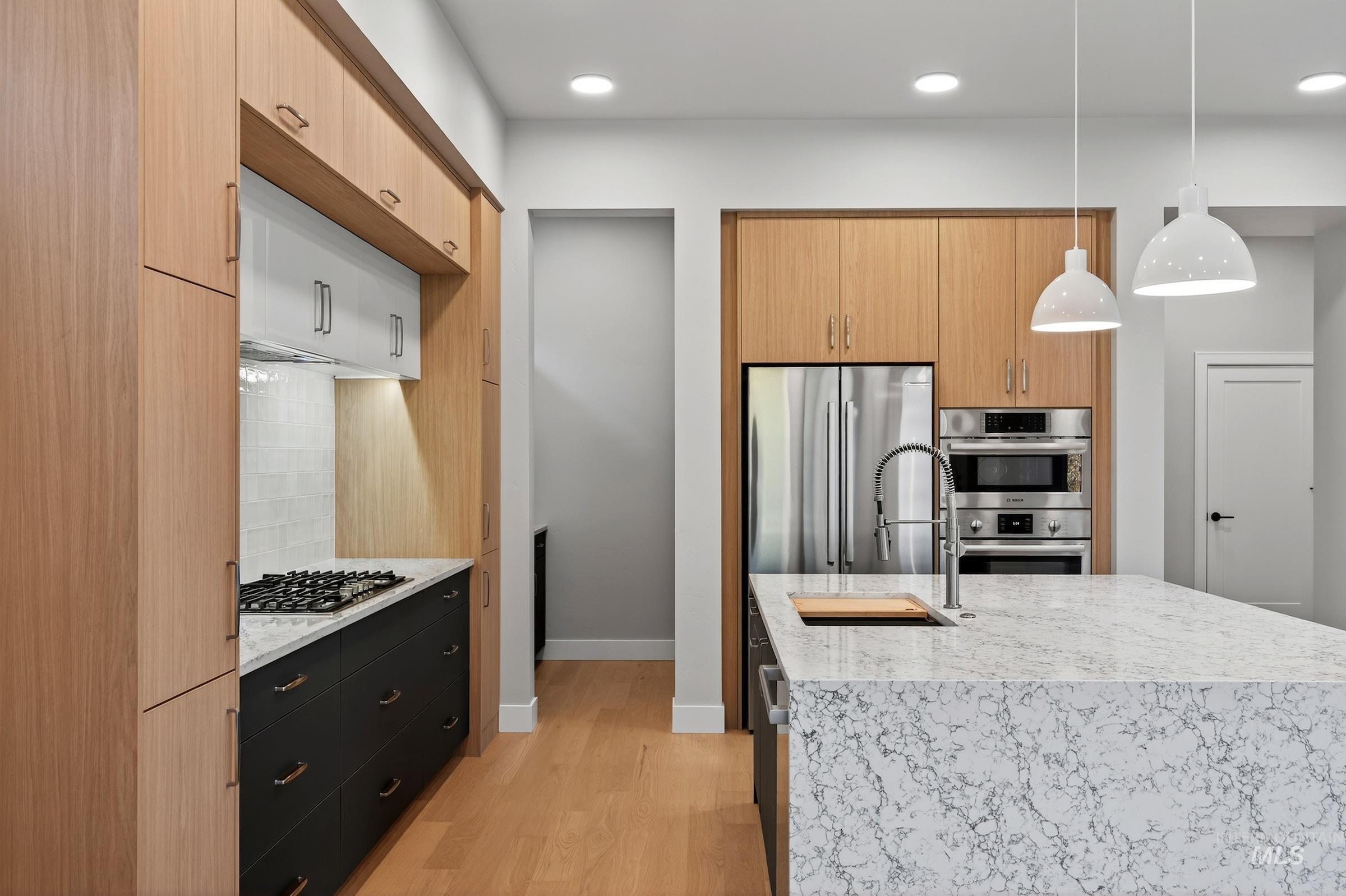 Kitchen with light stone countertops, decorative light fixtures, light wood-style floors, stainless steel appliances, and modern cabinets