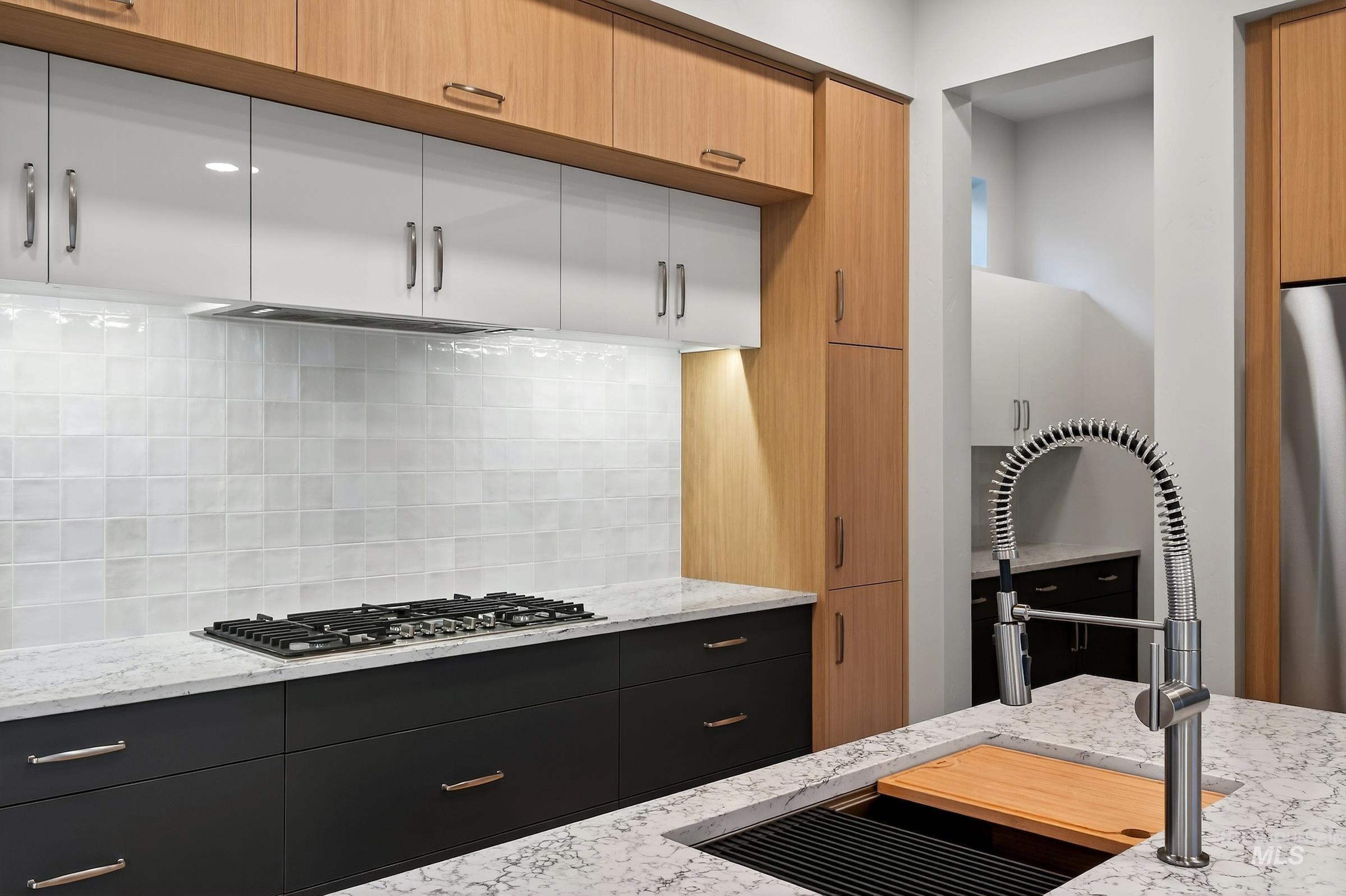 Kitchen with light stone counters, backsplash, stainless steel appliances, and modern cabinets